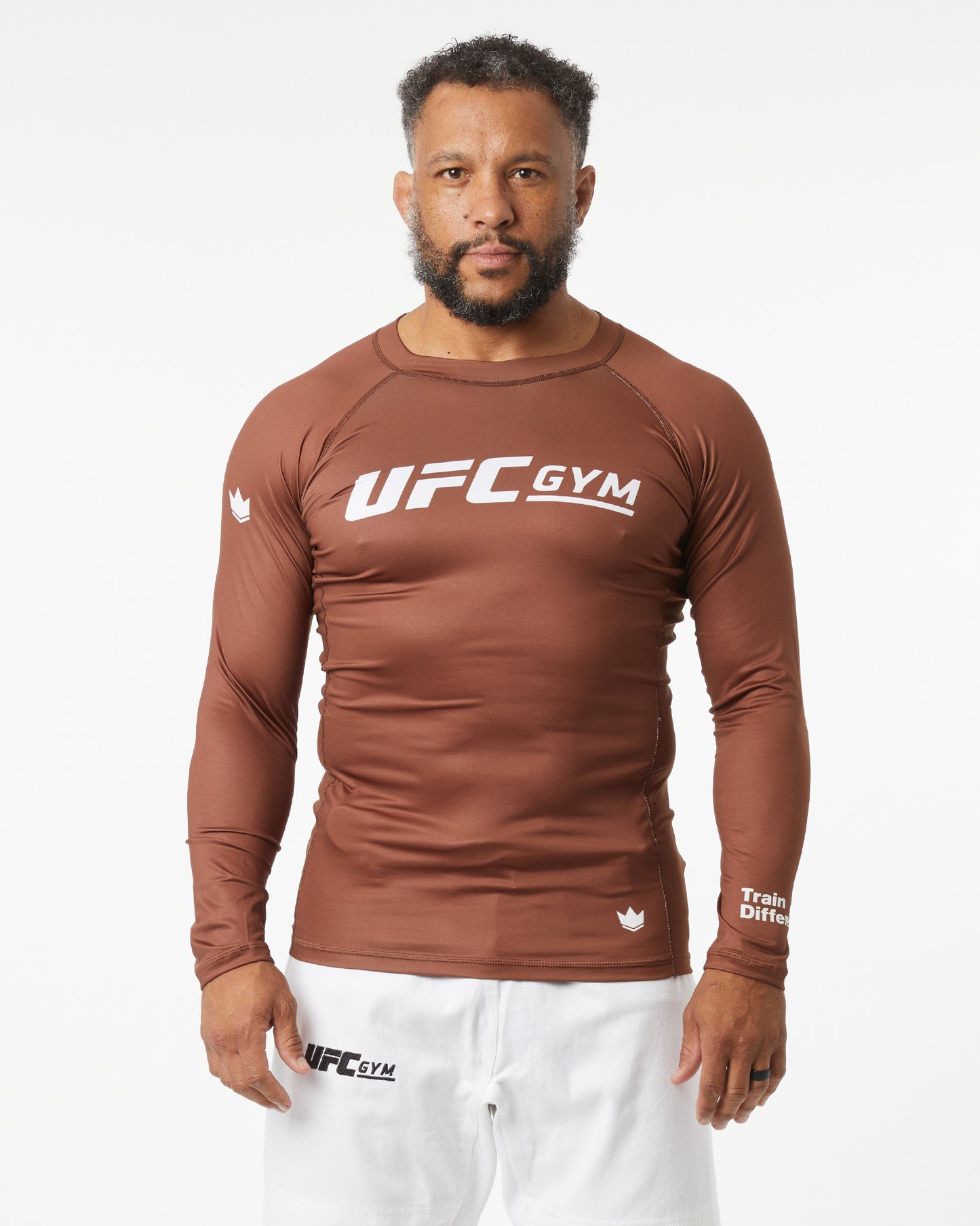 Man wearing a brown UFC Gym long-sleeve shirt and white shorts on a white background facing forward