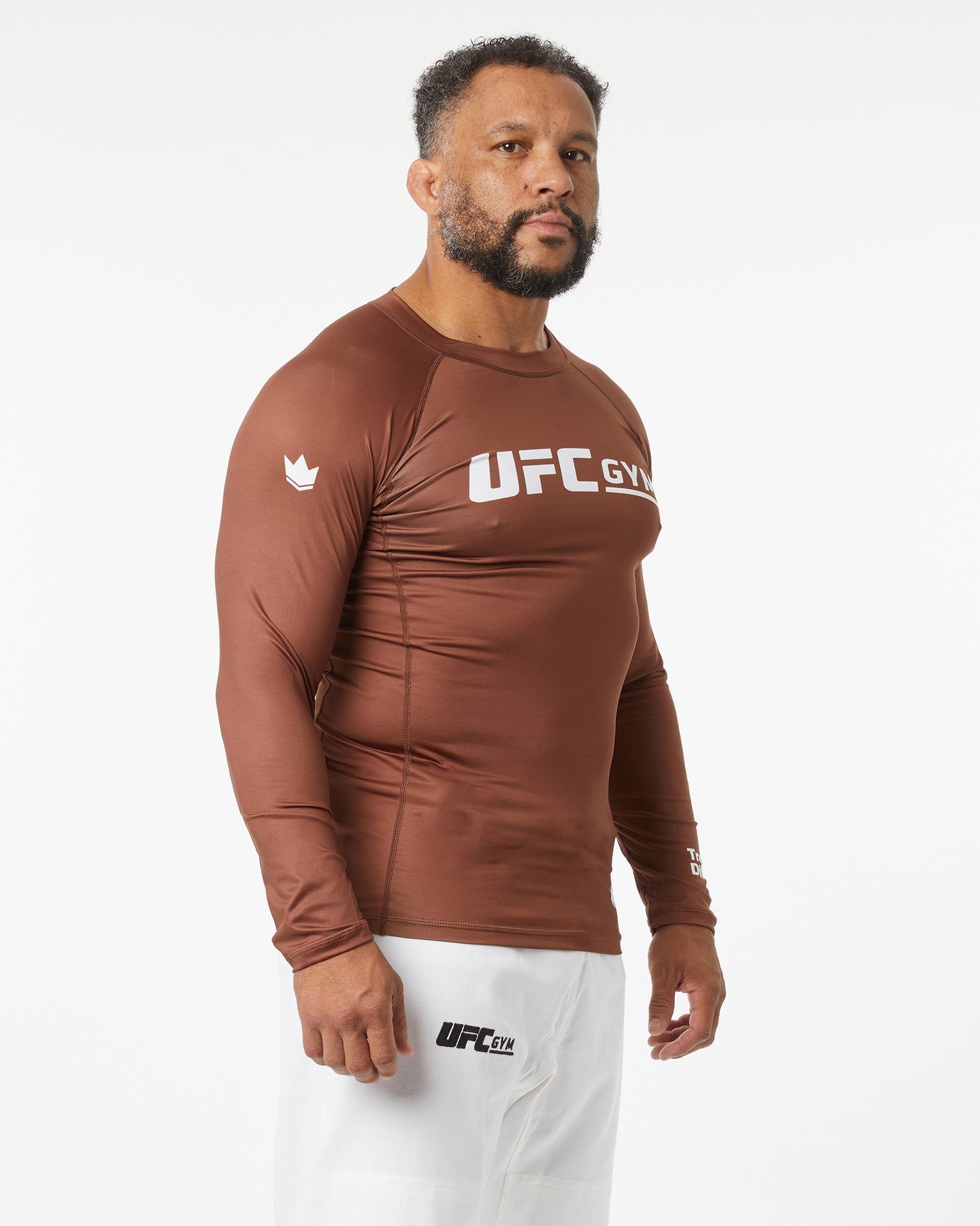 Man wearing a brown UFC Gym long-sleeve shirt on a white background facing right