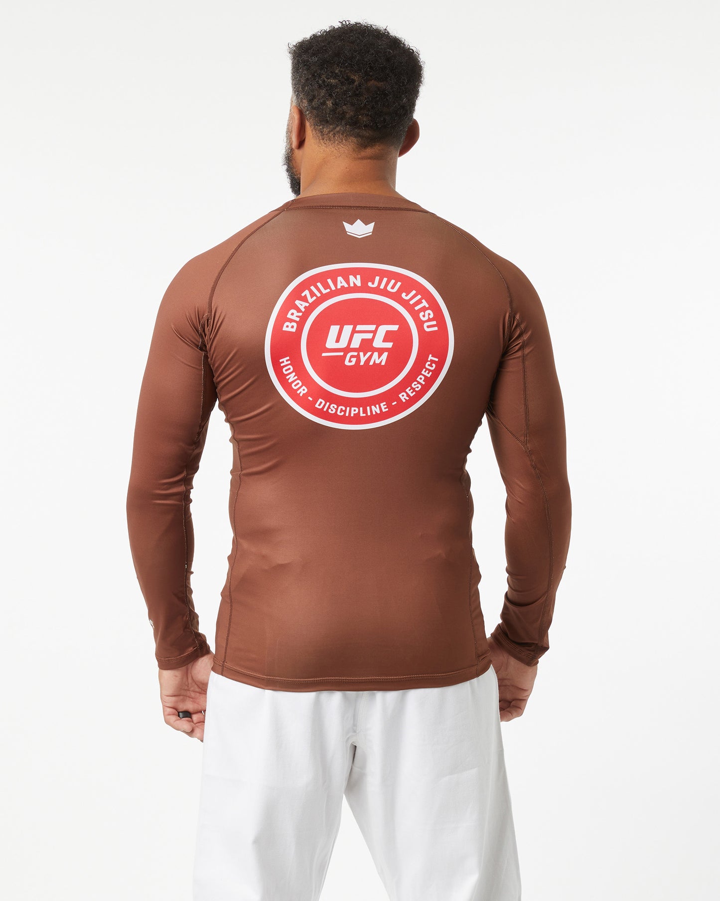 Person wearing a brown UFC Gym long-sleeve shirt with a red logo on the back against a white background facing backwards