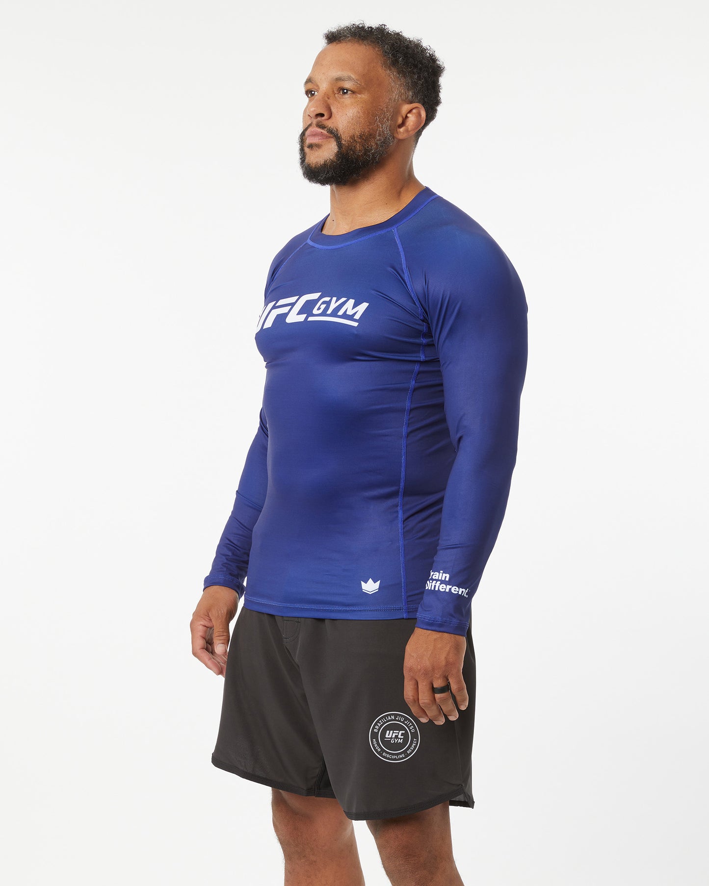 Man wearing a blue UFC Gym long-sleeve shirt and black shorts on a white background facing left