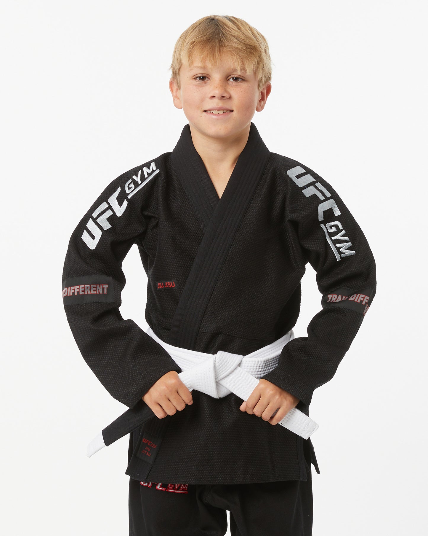 Child wearing a black UFC Gym gi with a white belt on a white background grasping their belt