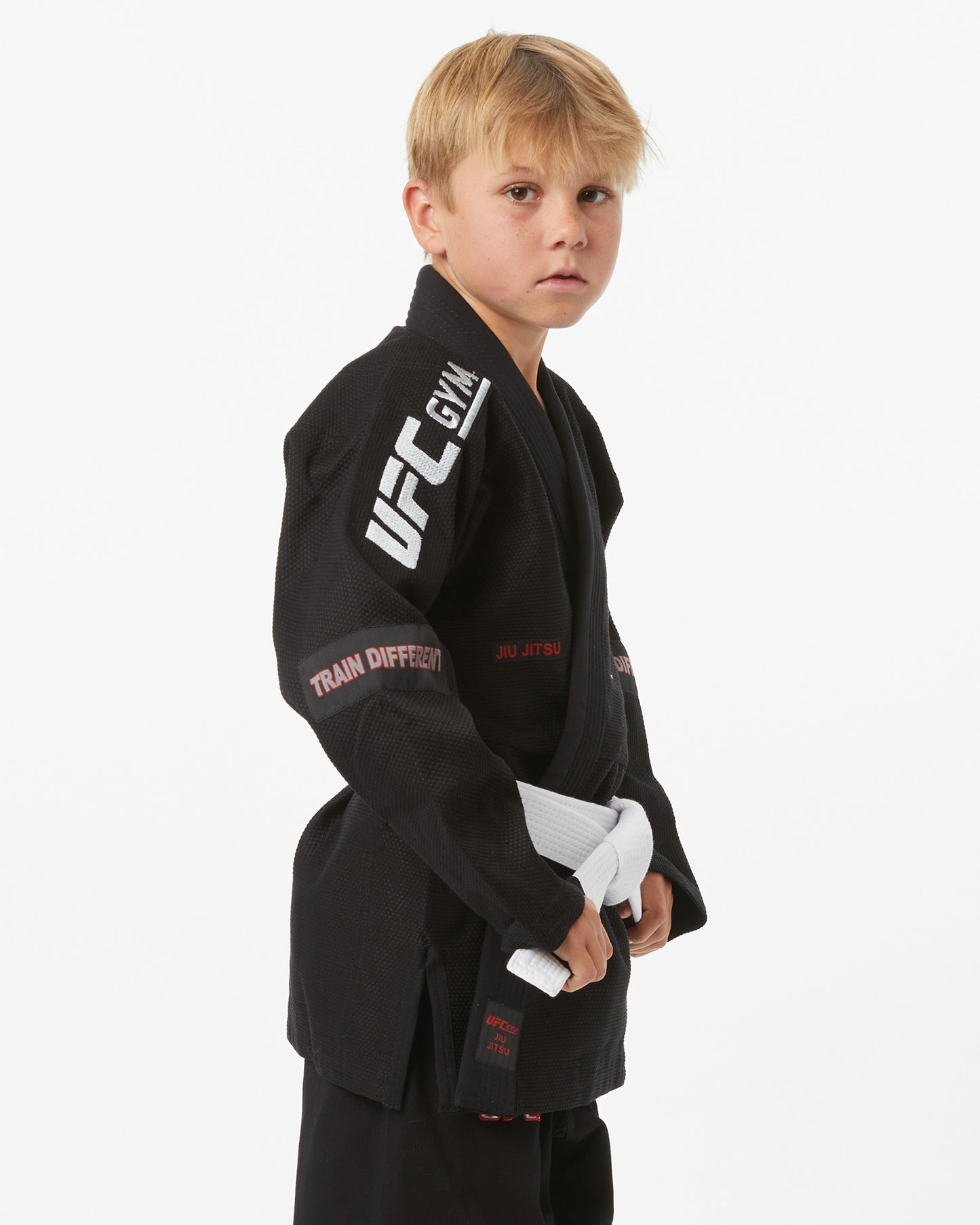 Child wearing a black UFC Gym gi with a white belt on a white background facing fully right looking forward