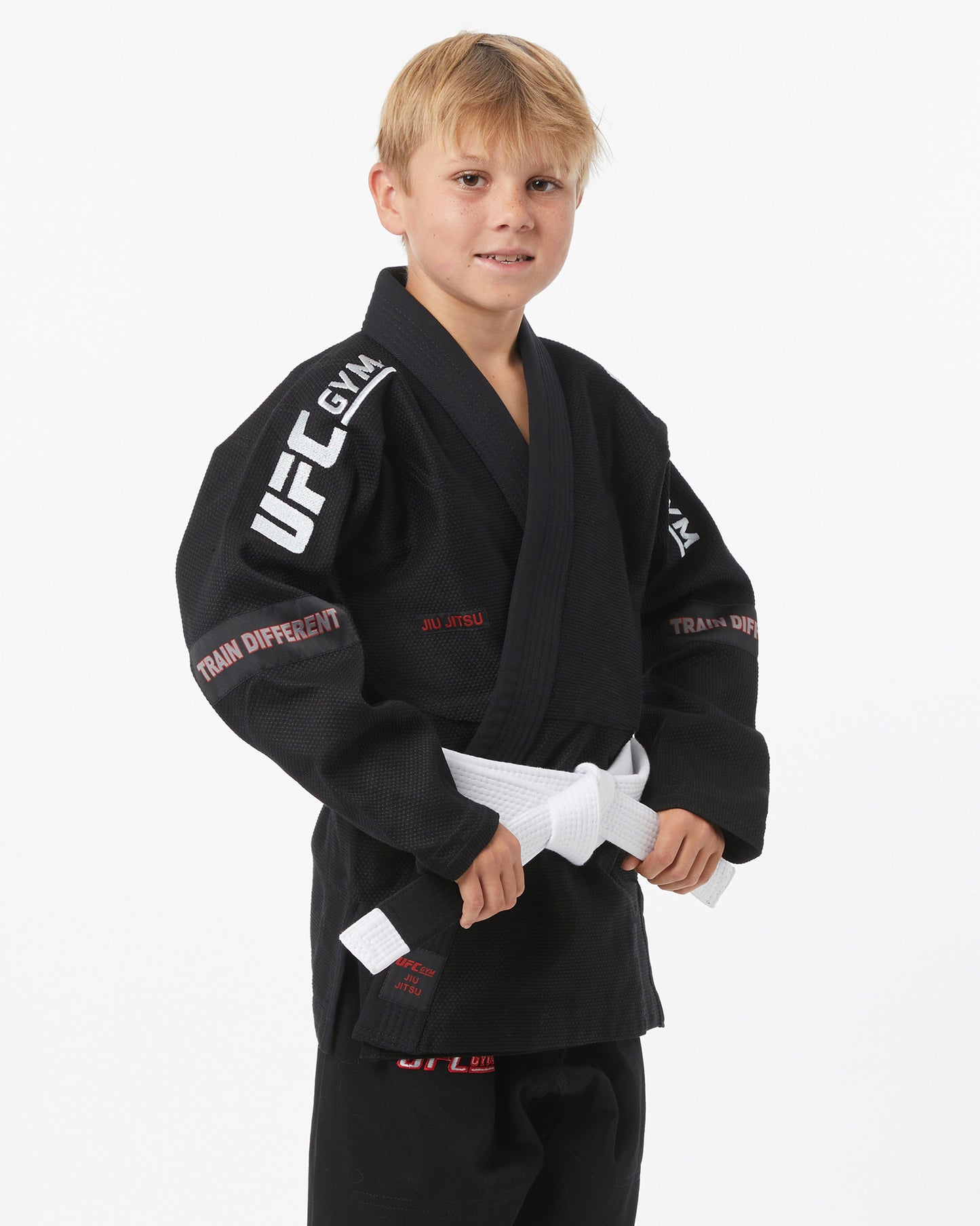 Child wearing a black UFC Gym gi with a white belt on a white background facing right looking forward