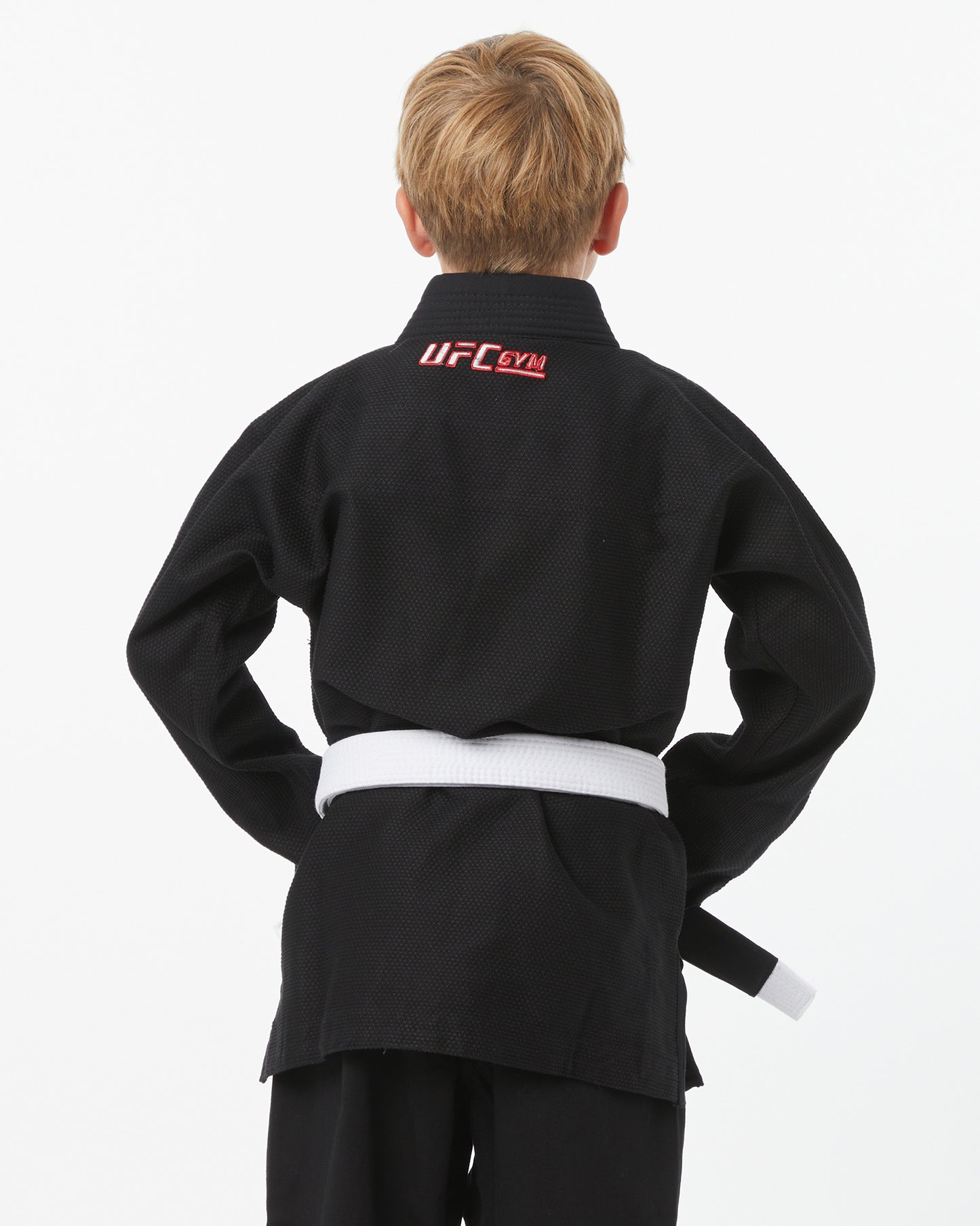 Child wearing a black UFC Gym gi with a white belt on a white background facing backwards