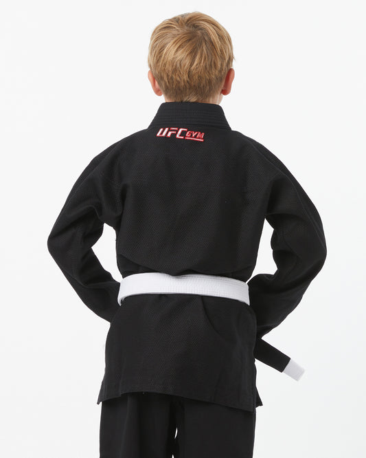 Child wearing a black UFC Gym gi with a white belt on a white background facing backwards