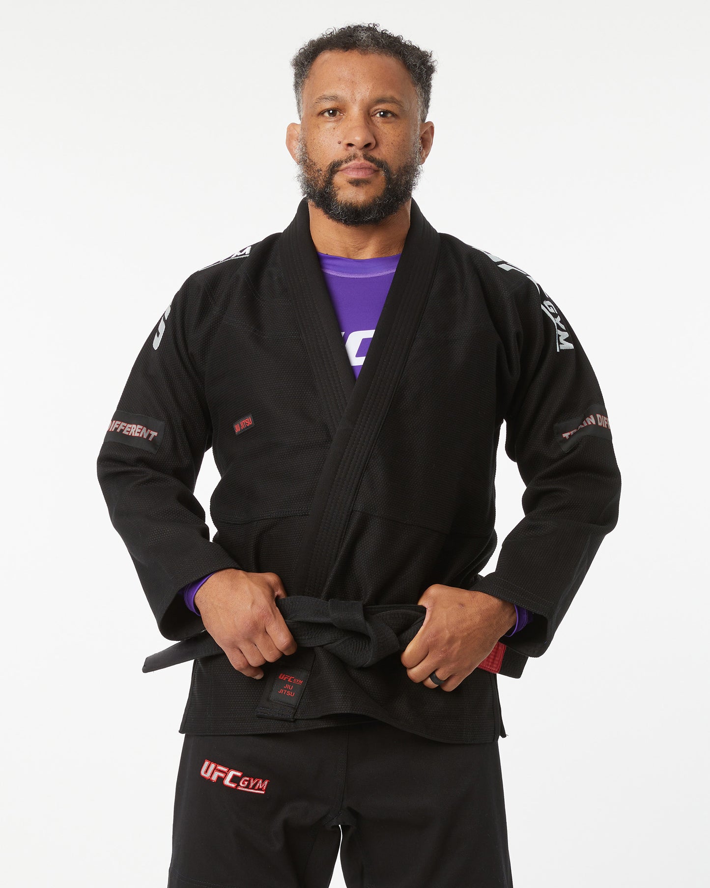 Person wearing a black UFC Gym gi on a white background with their hands on belt
