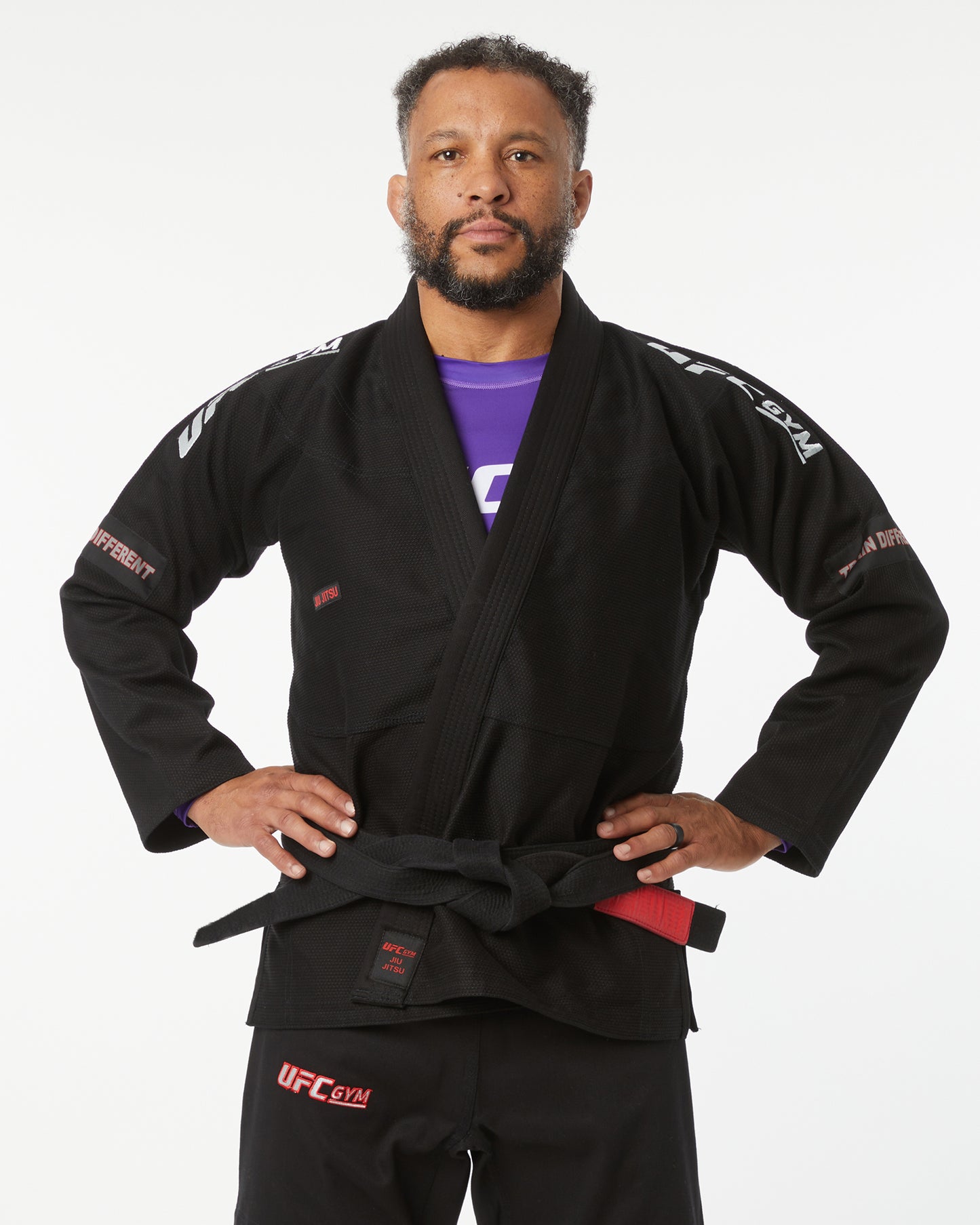 Man wearing a black UFC Gi with a purple shirt underneath on a white background hands on their sides