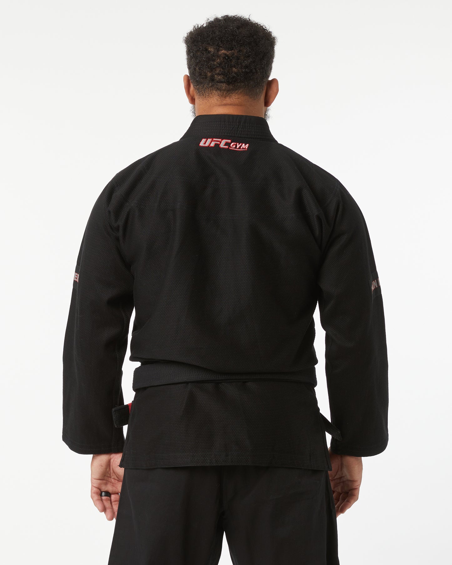 Person wearing a black UFC Gym jacket on a white background facing back