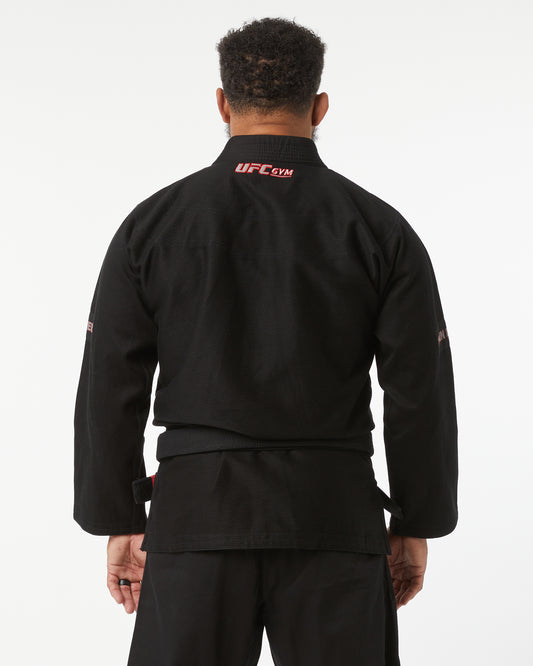 Person wearing a black UFC Gym jacket on a white background facing back
