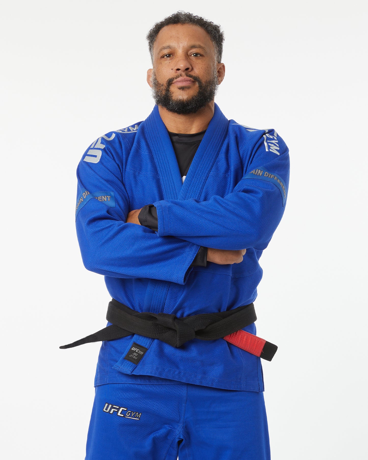 Person wearing a blue UFC gym uniform with a black belt on a white background, arms crossed