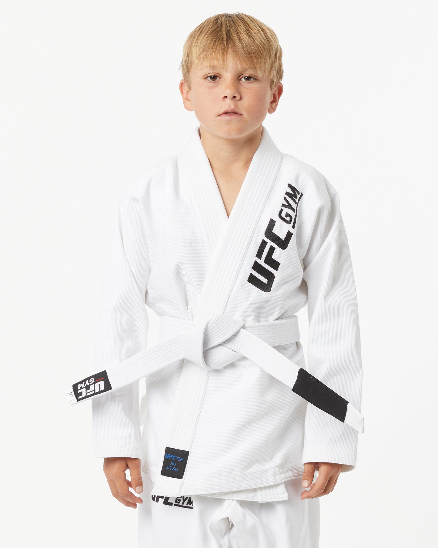 Child wearing a white UFC Gym gi with a white belt on a white background facing forward