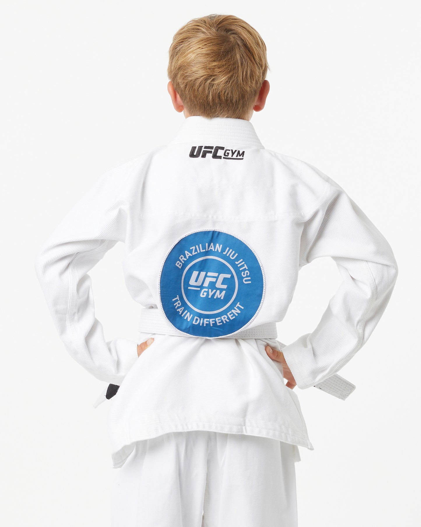 Child wearing a white UFC Gym gi with a blue patch on the back of the gi a white background facing backward
