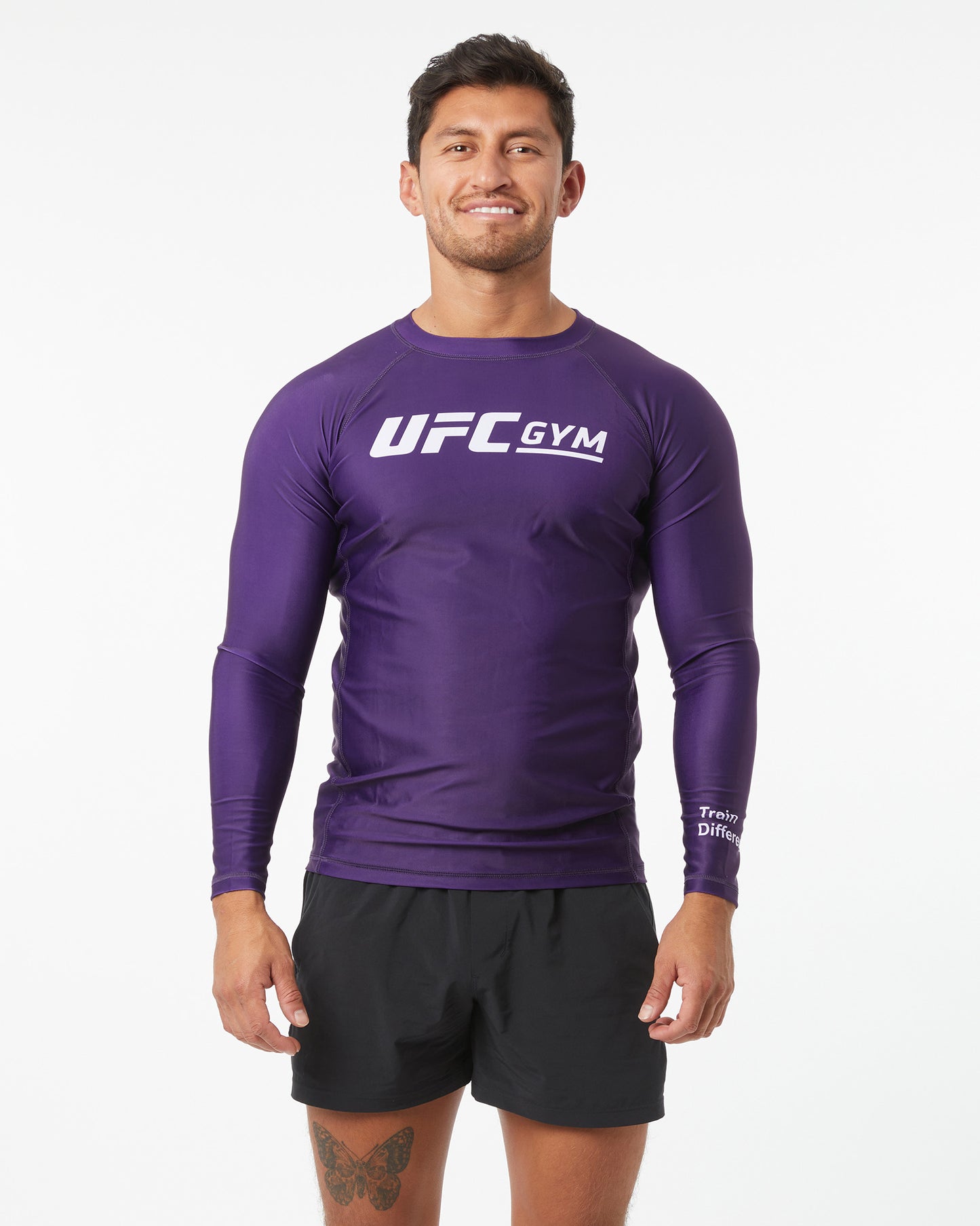 Man wearing a purple UFC Gym long-sleeve shirt and black shorts on a white background facing forward arms down