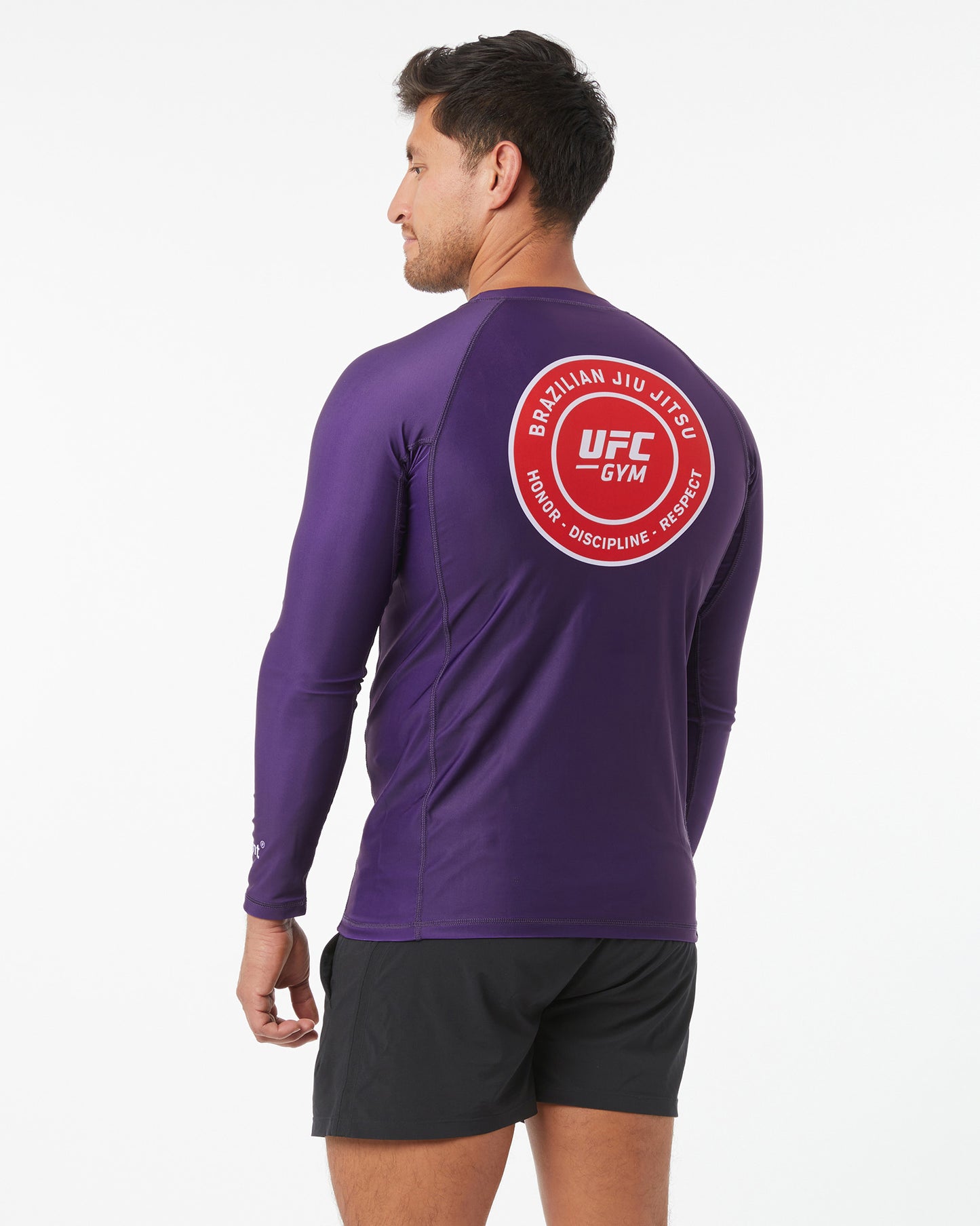 Person wearing a purple UFC Gym long-sleeve shirt with a red logo on the back, facing back looking left