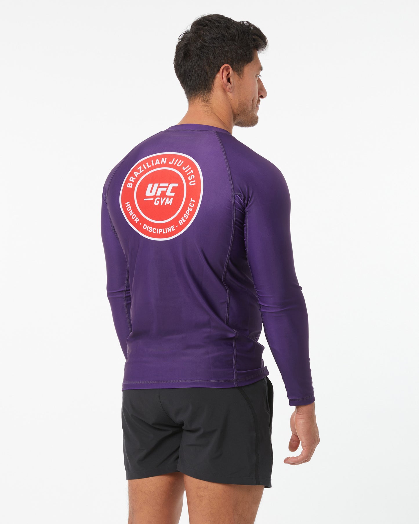 Person wearing a purple athletic shirt with UFC Gym logo on the back against a white background facing backwards looking to the right