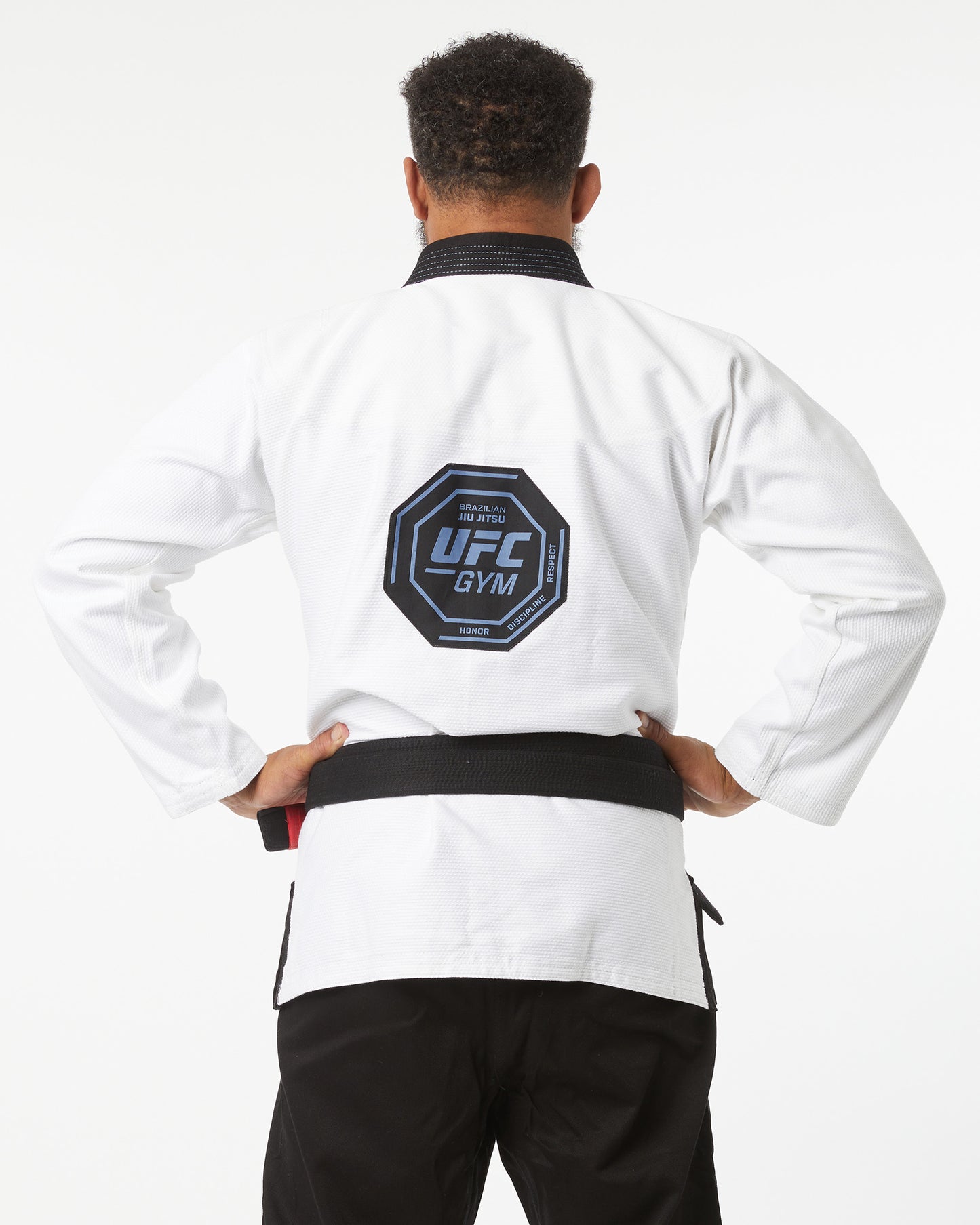Person wearing a white UFC Gym jacket with a black belt on a white background back logo showing