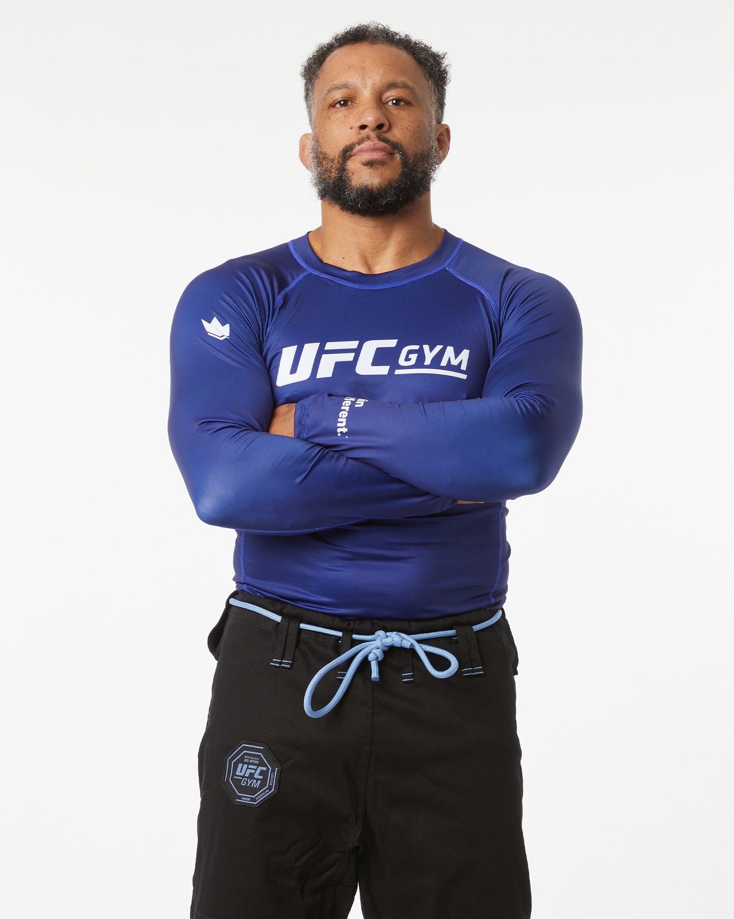 Person wearing a blue UFC Gym shirt with arms crossed on a white background