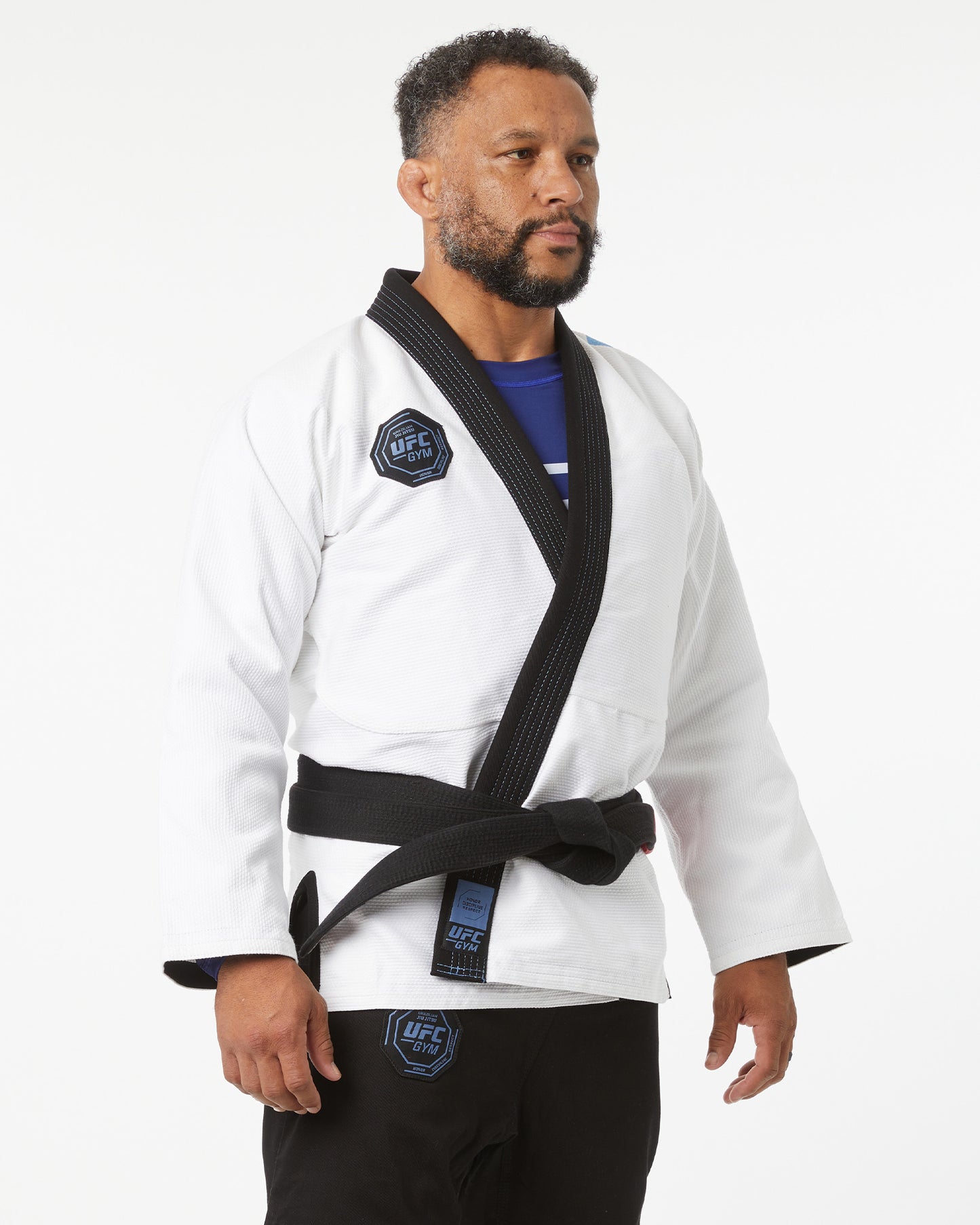Person wearing a white martial arts uniform with black belt on a white background facing slightly right