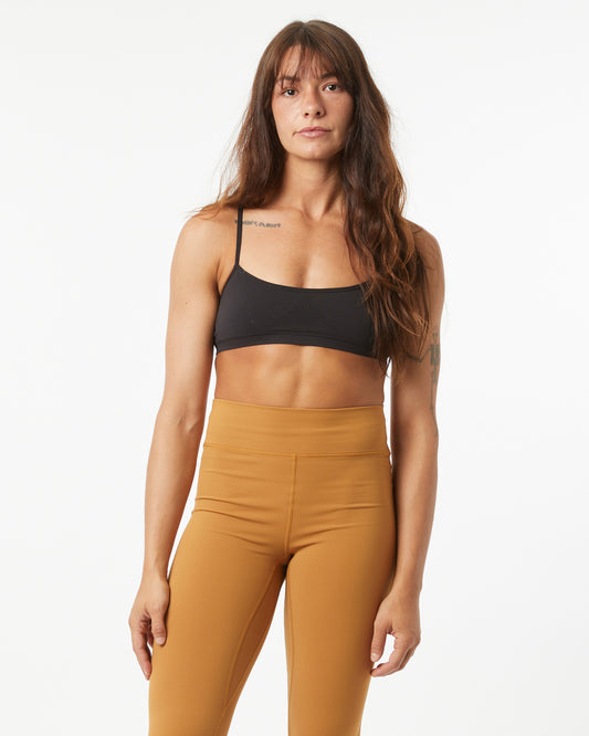 Woman wearing a black sports bra and bronze leggings on a white background