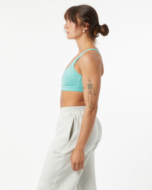 Woman wearing a light blue sports bra and white pants on a white background
