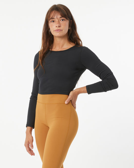 Woman wearing a black long-sleeve crop-top and bronze leggings on a white background