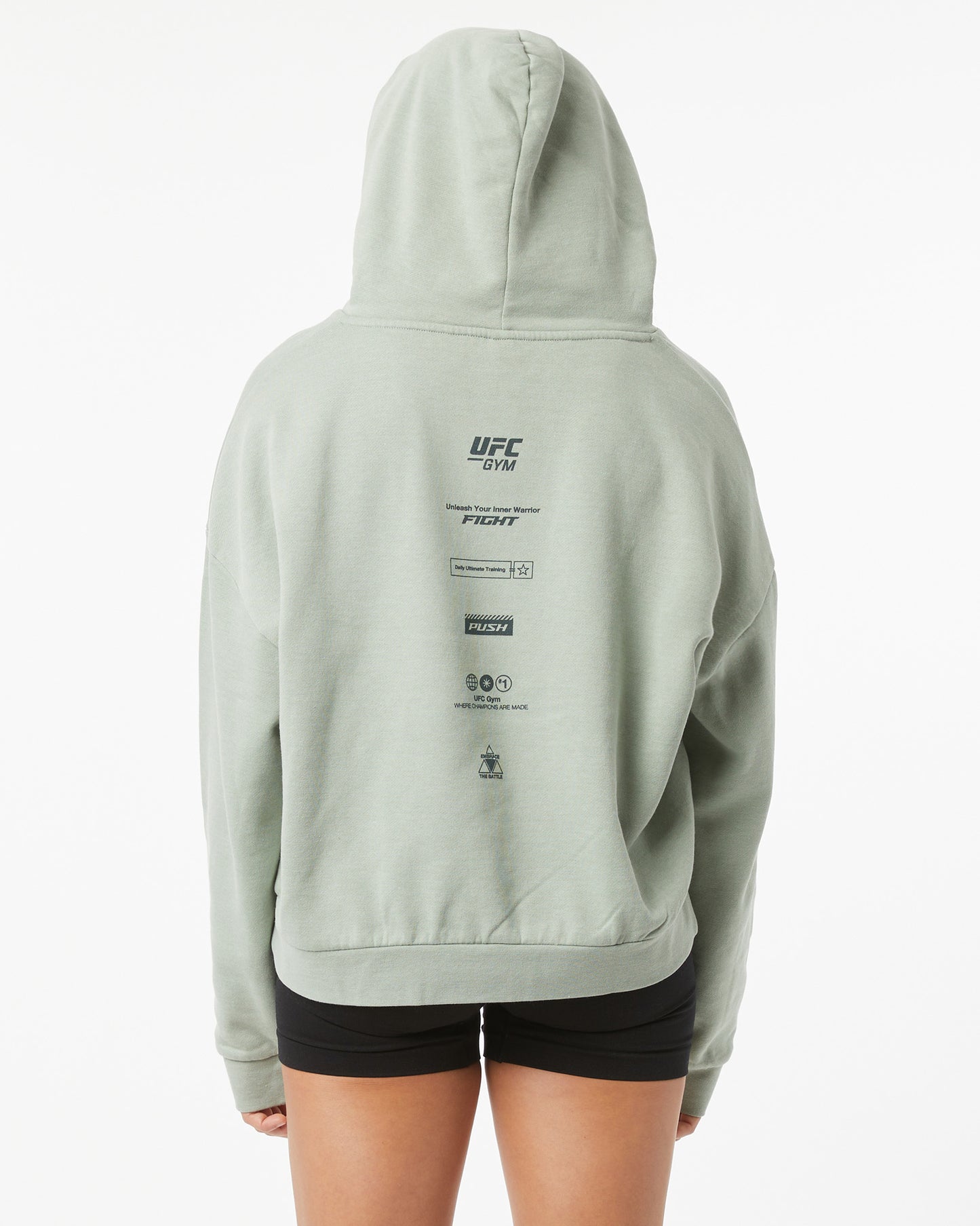 Woman wearing a light green UFC hoodie with branding on the back on a white background facing backwards