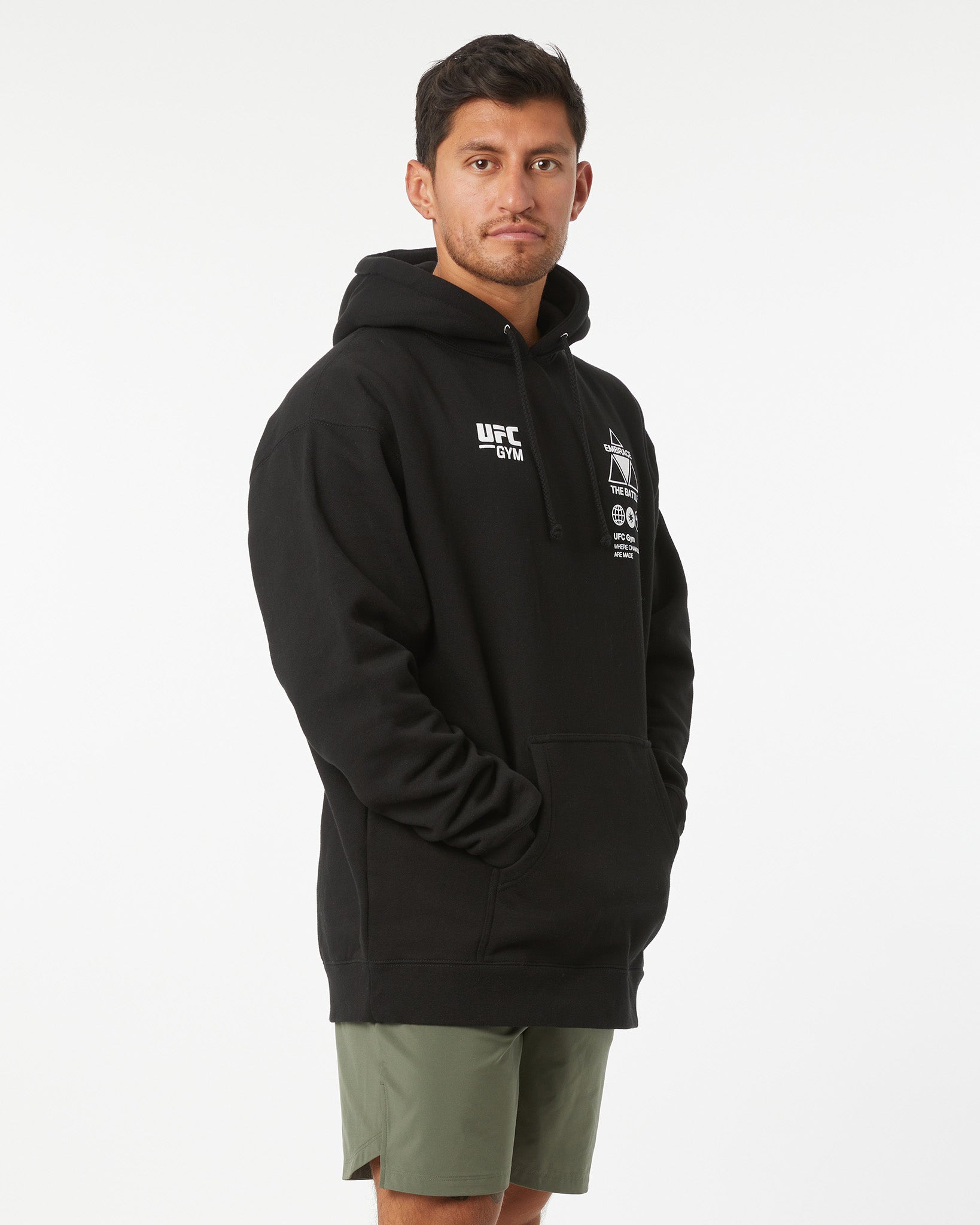 Man wearing a black UFC hoodie with a white logo on a white background facing right looking forward