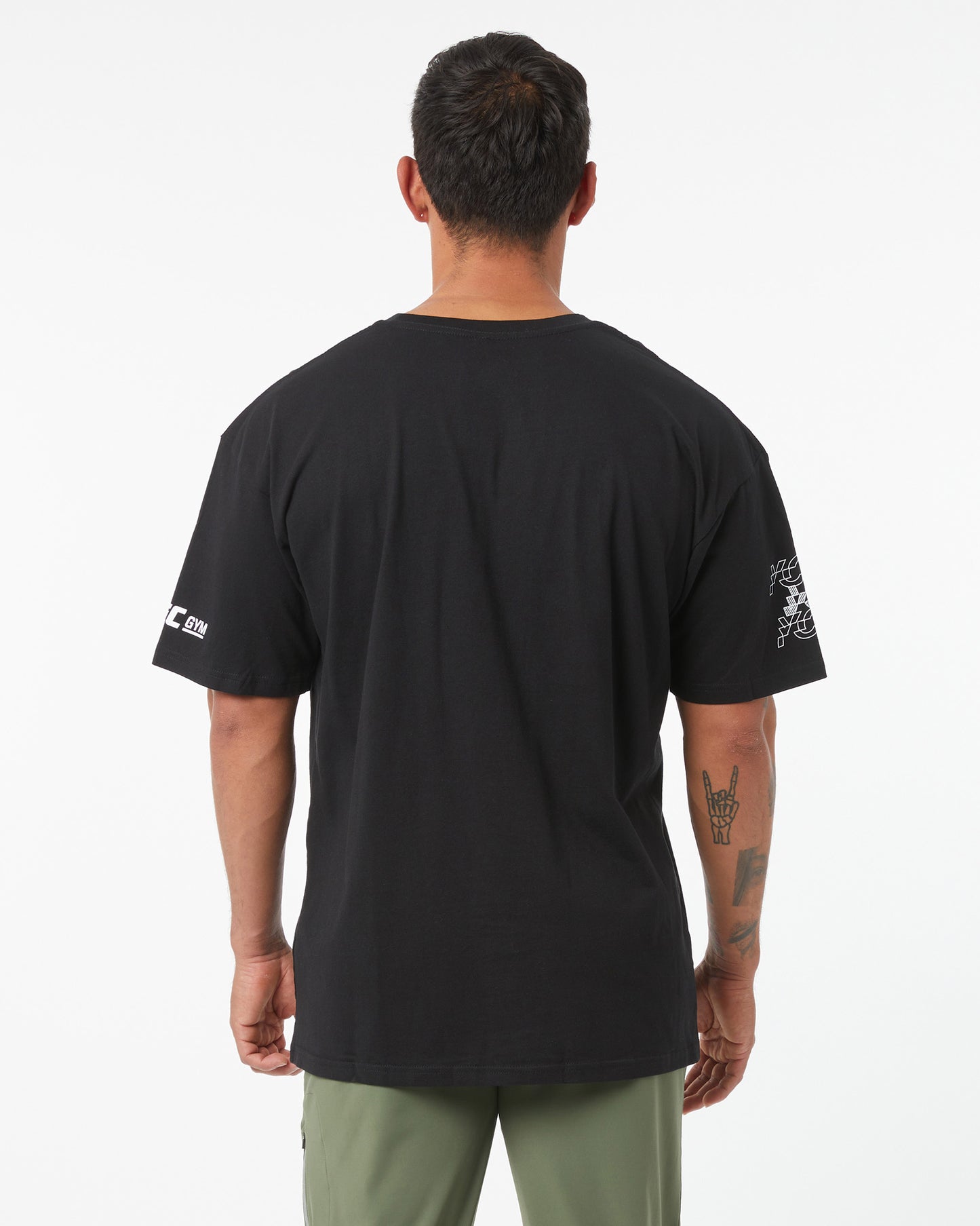 Man wearing a black t-shirt with logos on the back and sleeves, standing against a white background.