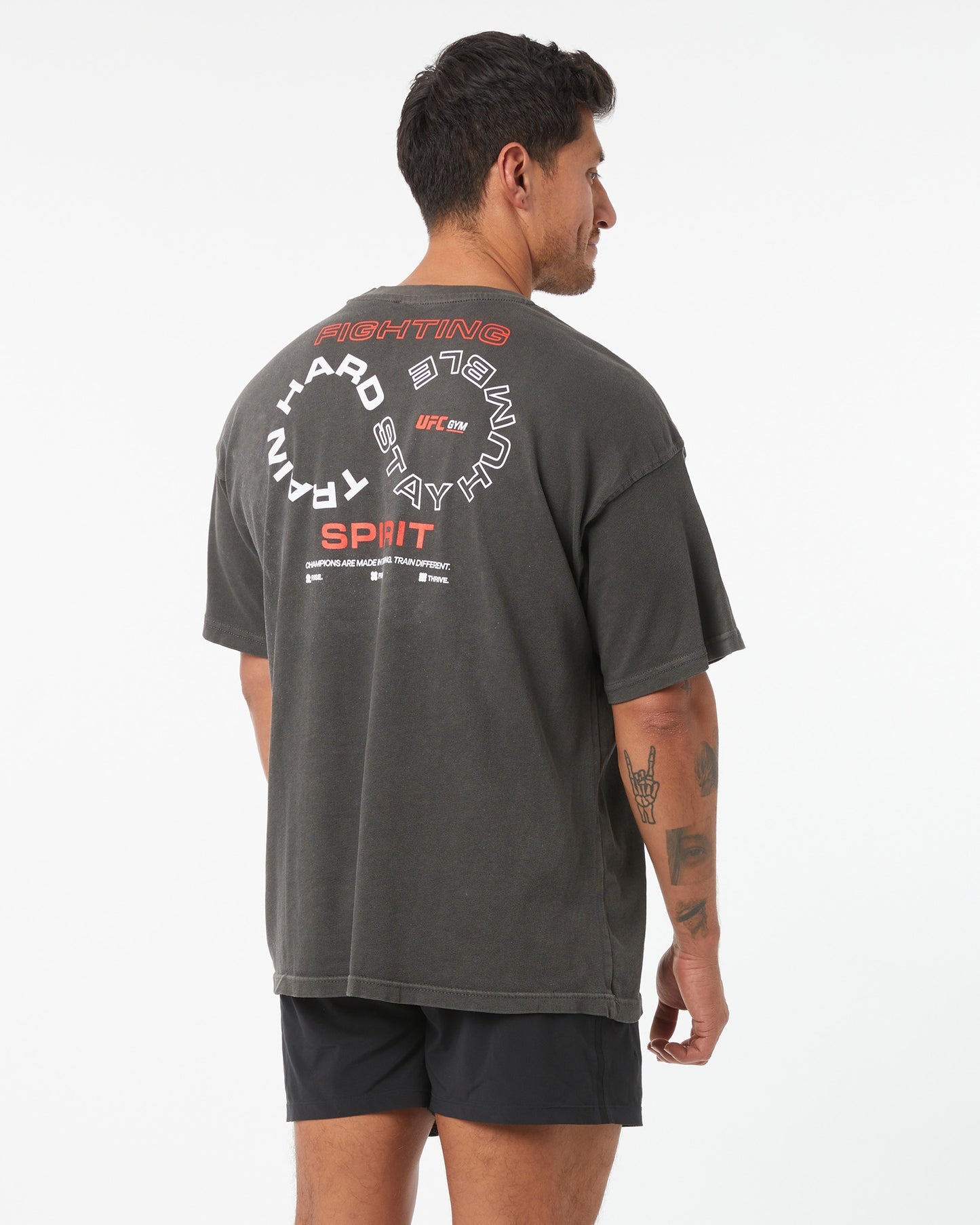 Person wearing a dark gray t-shirt with text on the back, standing against a white background