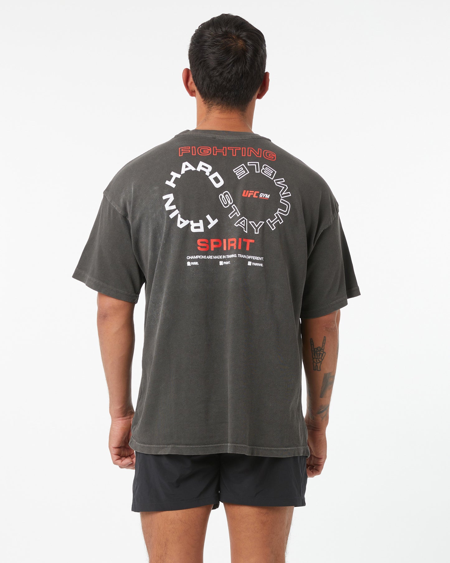 Person wearing a dark gray t-shirt with text on the back, standing against a white background