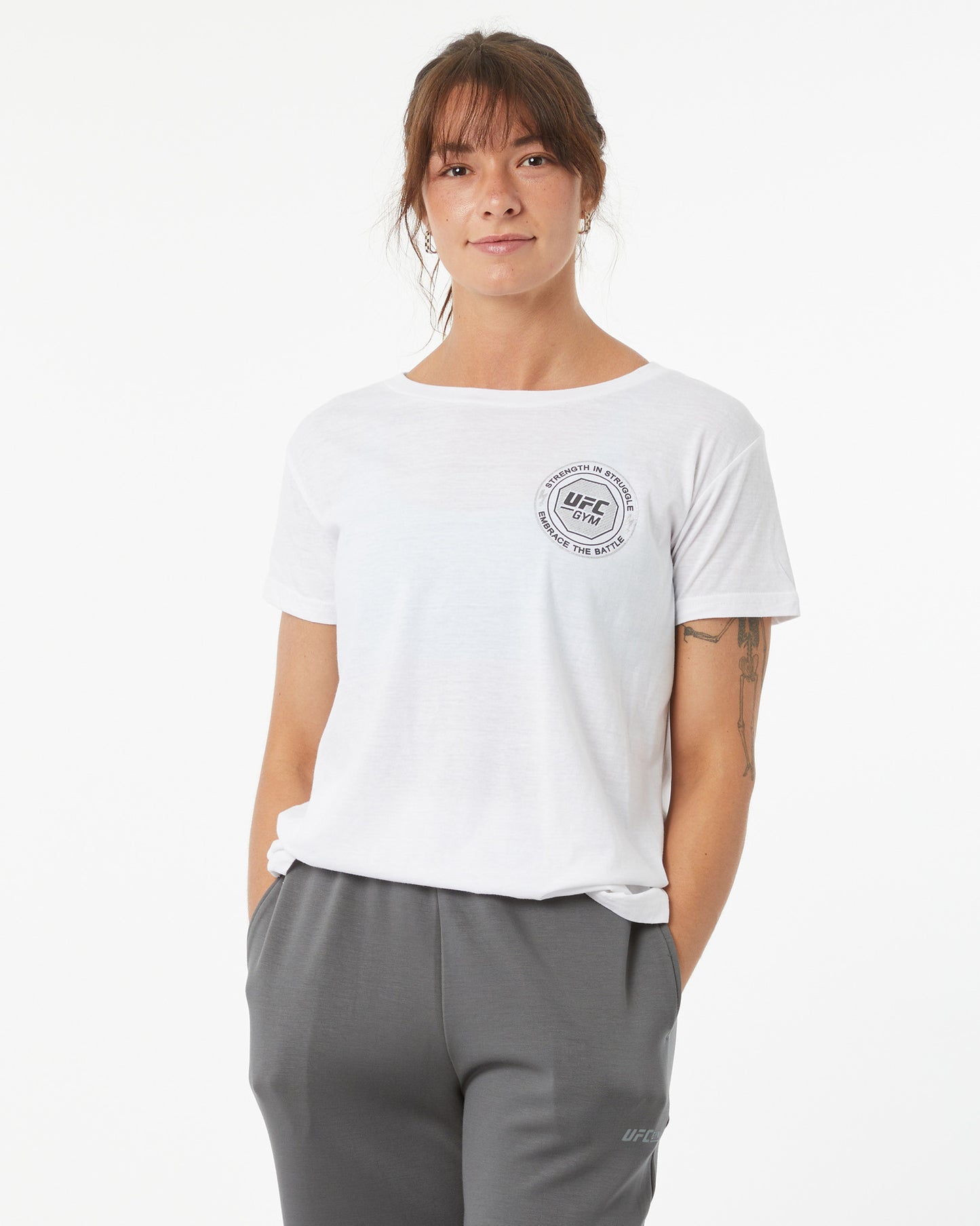 Person wearing a white t-shirt with a logo and gray pants on a white background facing forward