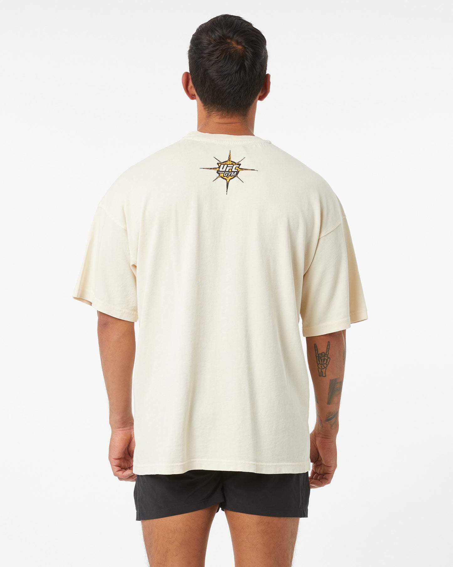 Man wearing a beige t-shirt with a logo on the back against a white background facing away