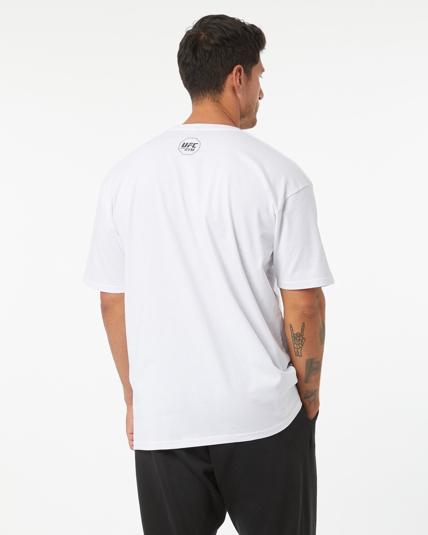Man wearing a white t-shirt with a logo on the back, standing against a plain background