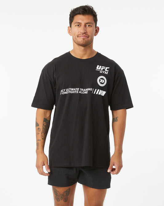 Man wearing black t-shirt with UFC GYM logo that says "only ultimate training no one fights alone" facing forward on a white background