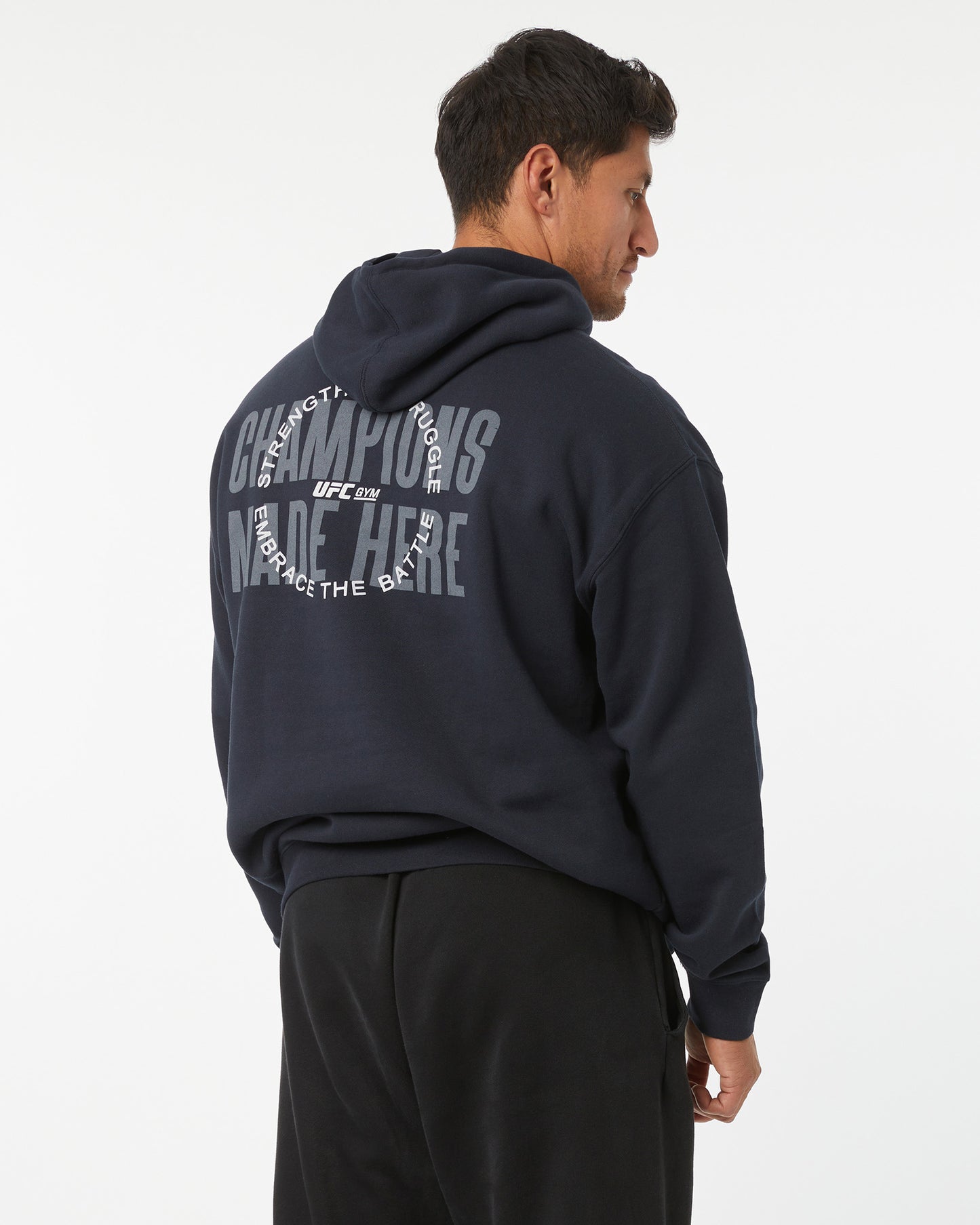 Man wearing a black hoodie with train different, strength in struggle text with a UFC GYM logo on the back, standing against a white background