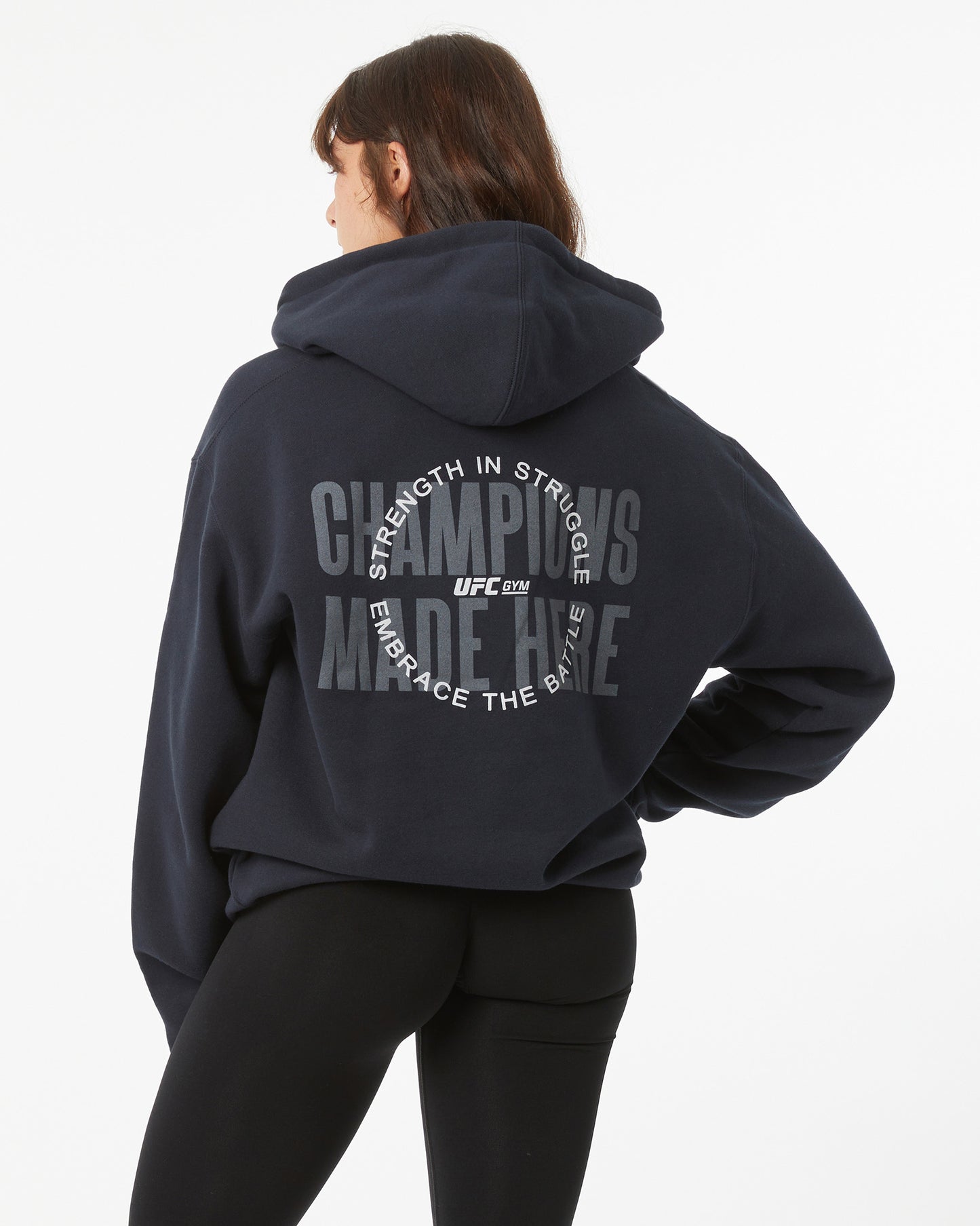 Woman wearing a black hoodie with train different, strength in struggle text with a UFC GYM logo on the back, against a white background