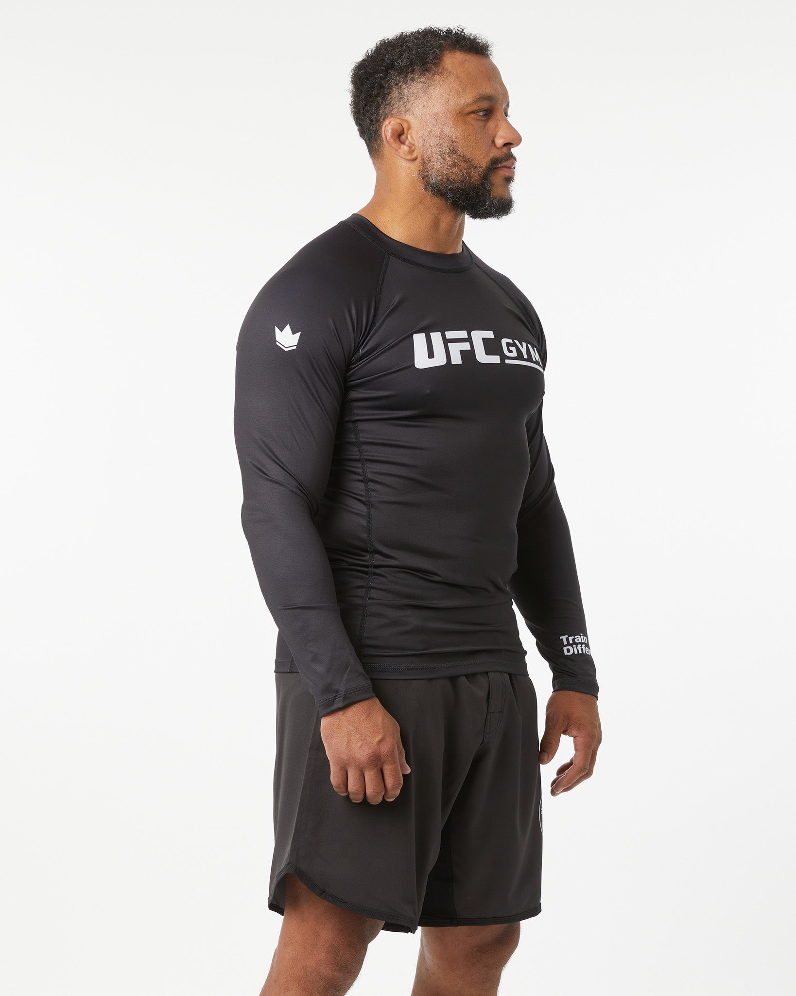 Man wearing a black UFC Gym long-sleeve shirt and shorts on a white background in a left-facing angle