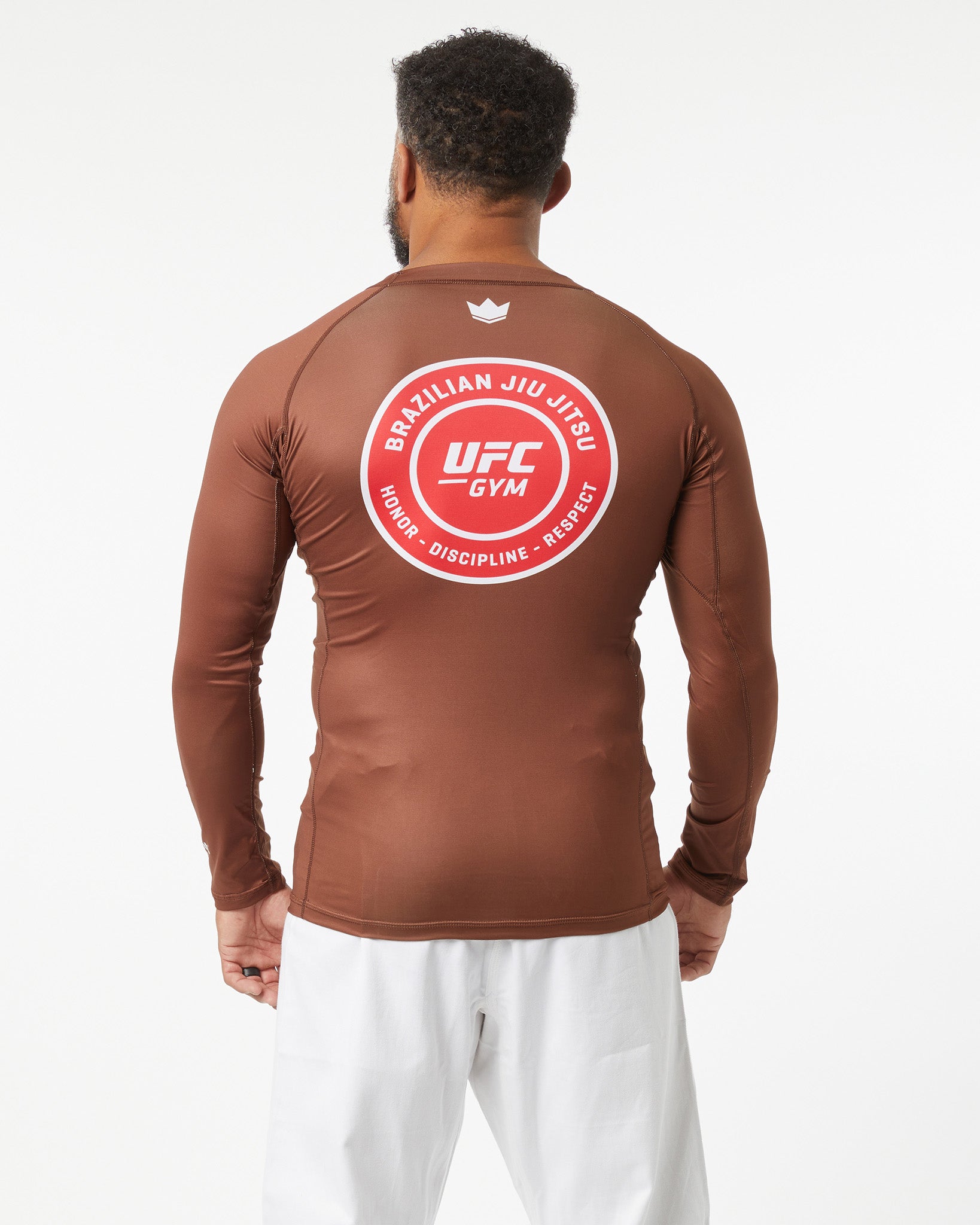 Person wearing a brown UFC Gym long-sleeve shirt with a red logo on the back against a white background facing backwards