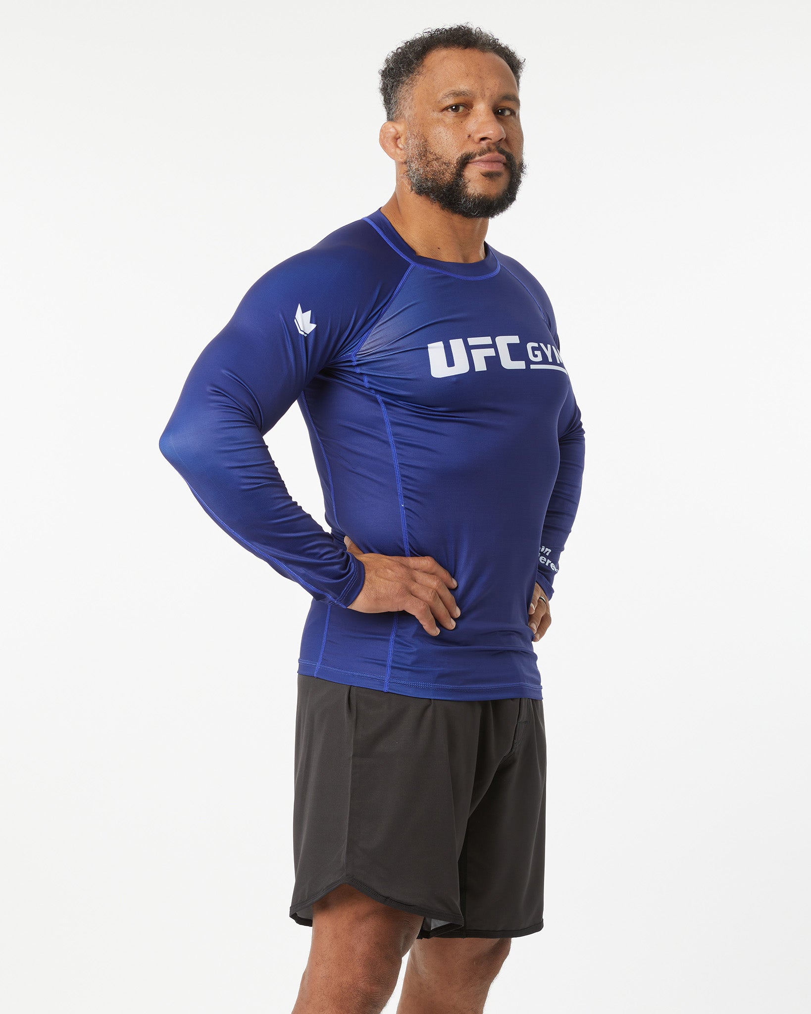 Man wearing a blue UFC Gym long-sleeve shirt on a white background facing right