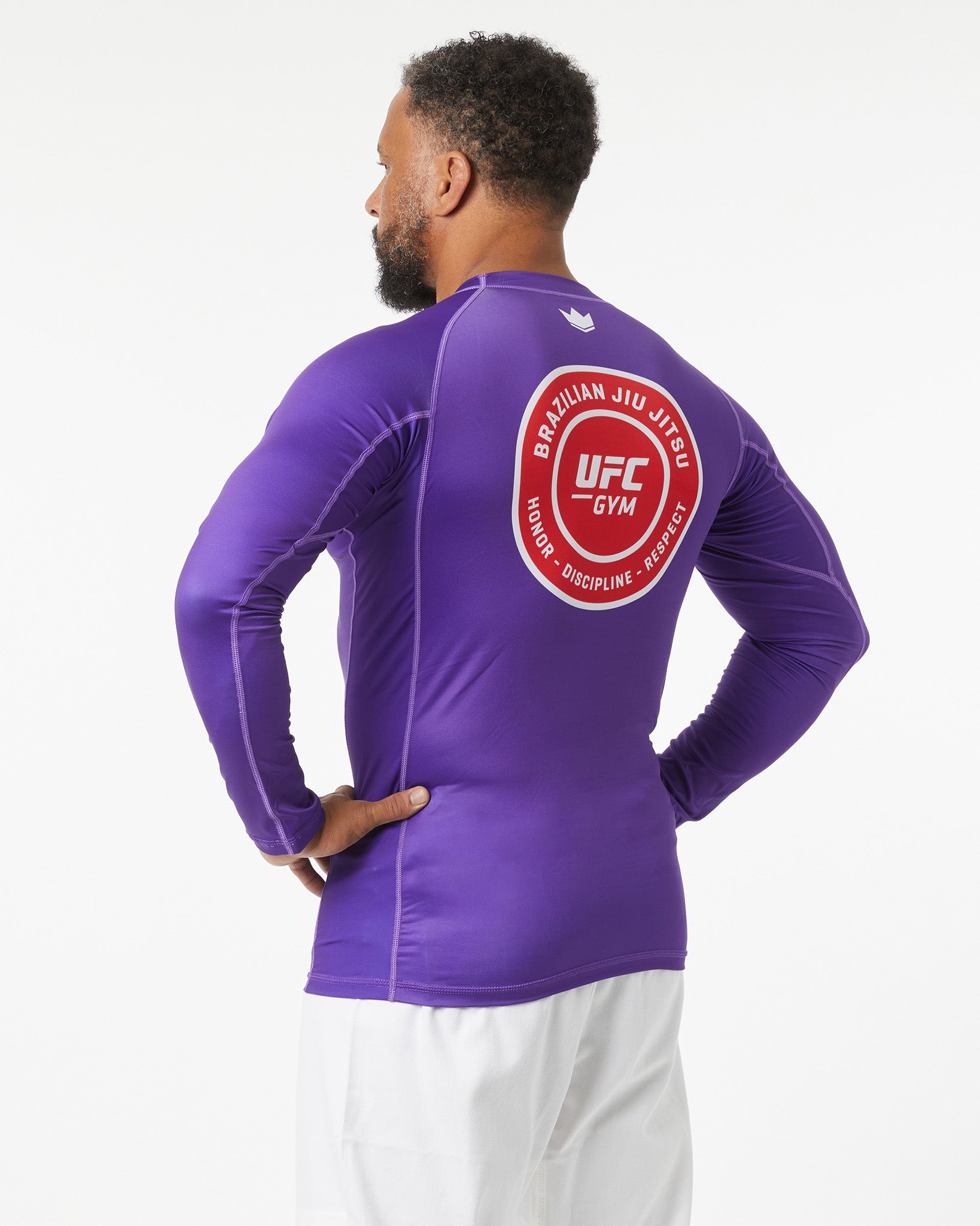 Person wearing a purple UFC Gym long-sleeve shirt with a logo on the back against a white background