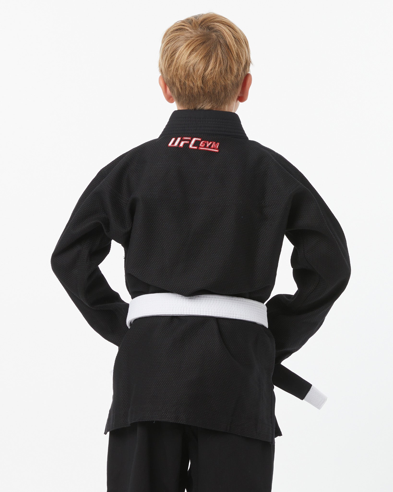 Child wearing a black UFC Gym gi with a white belt on a white background facing backwards