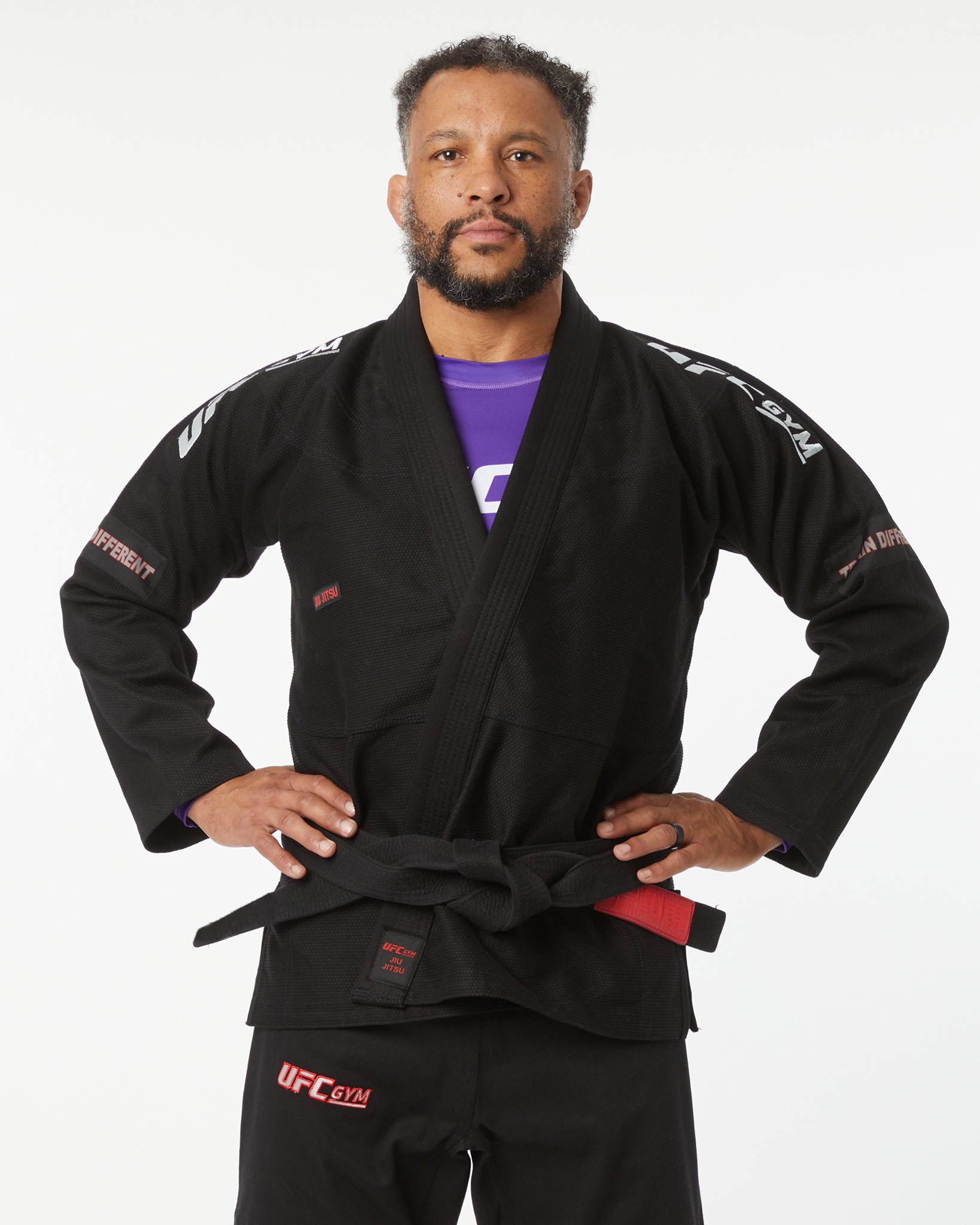 Man wearing a black UFC Gi with a purple shirt underneath on a white background hands on their sides