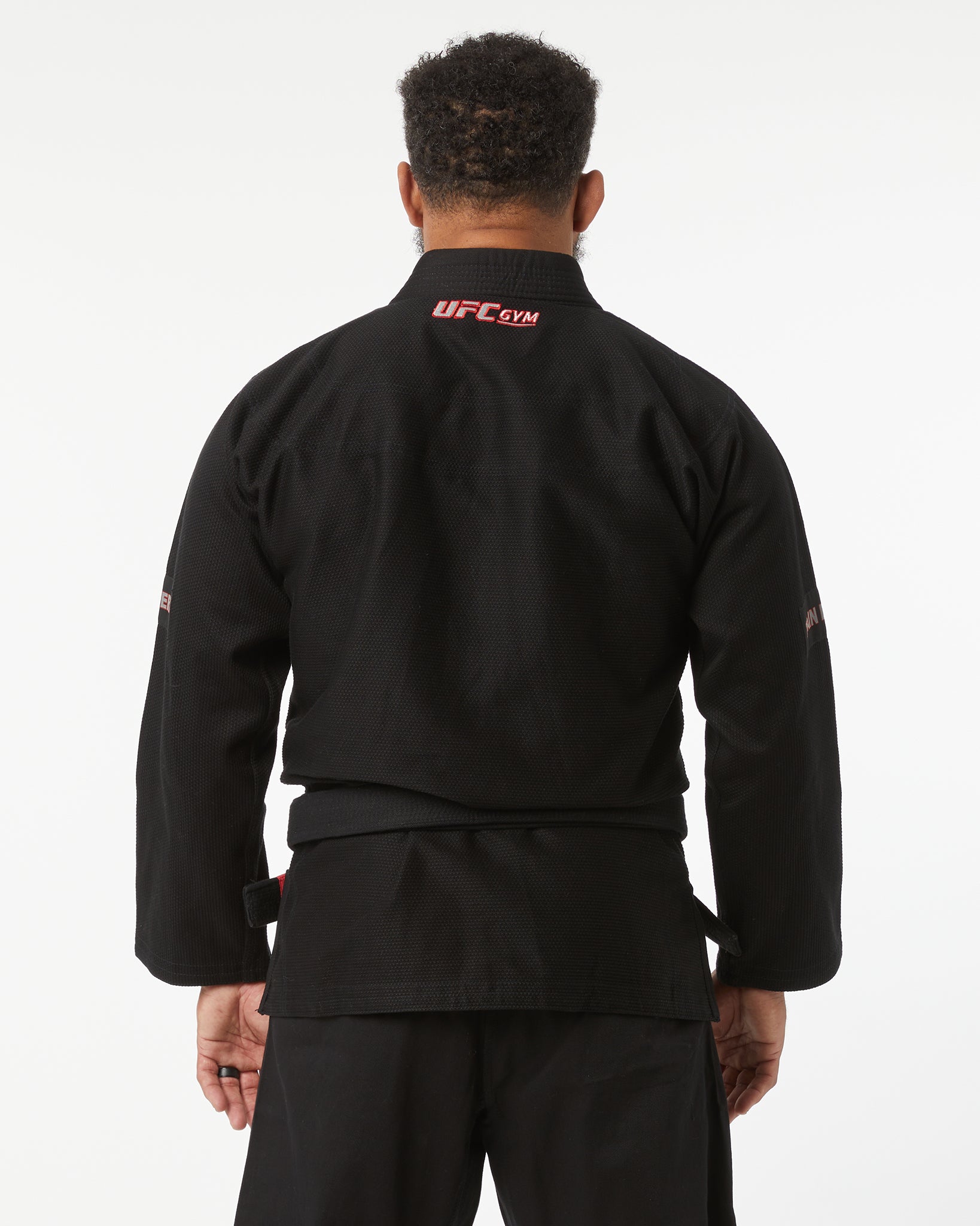Person wearing a black UFC Gym jacket on a white background facing back