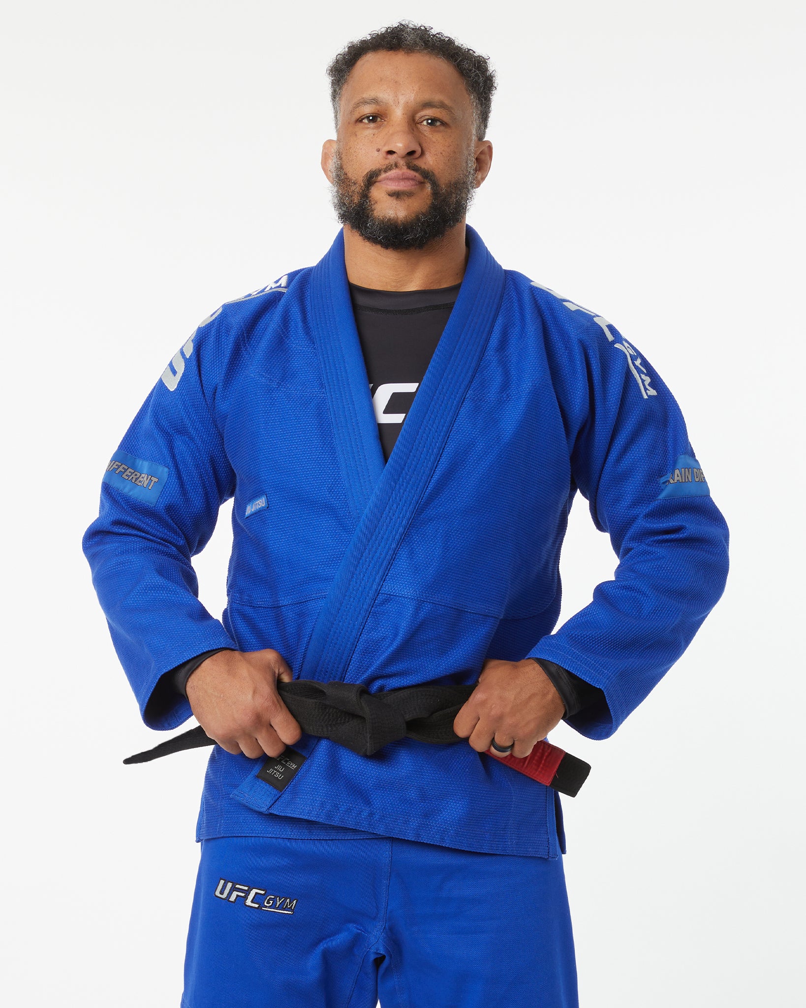 Person wearing a blue UFC gi with a white background with hands on belt