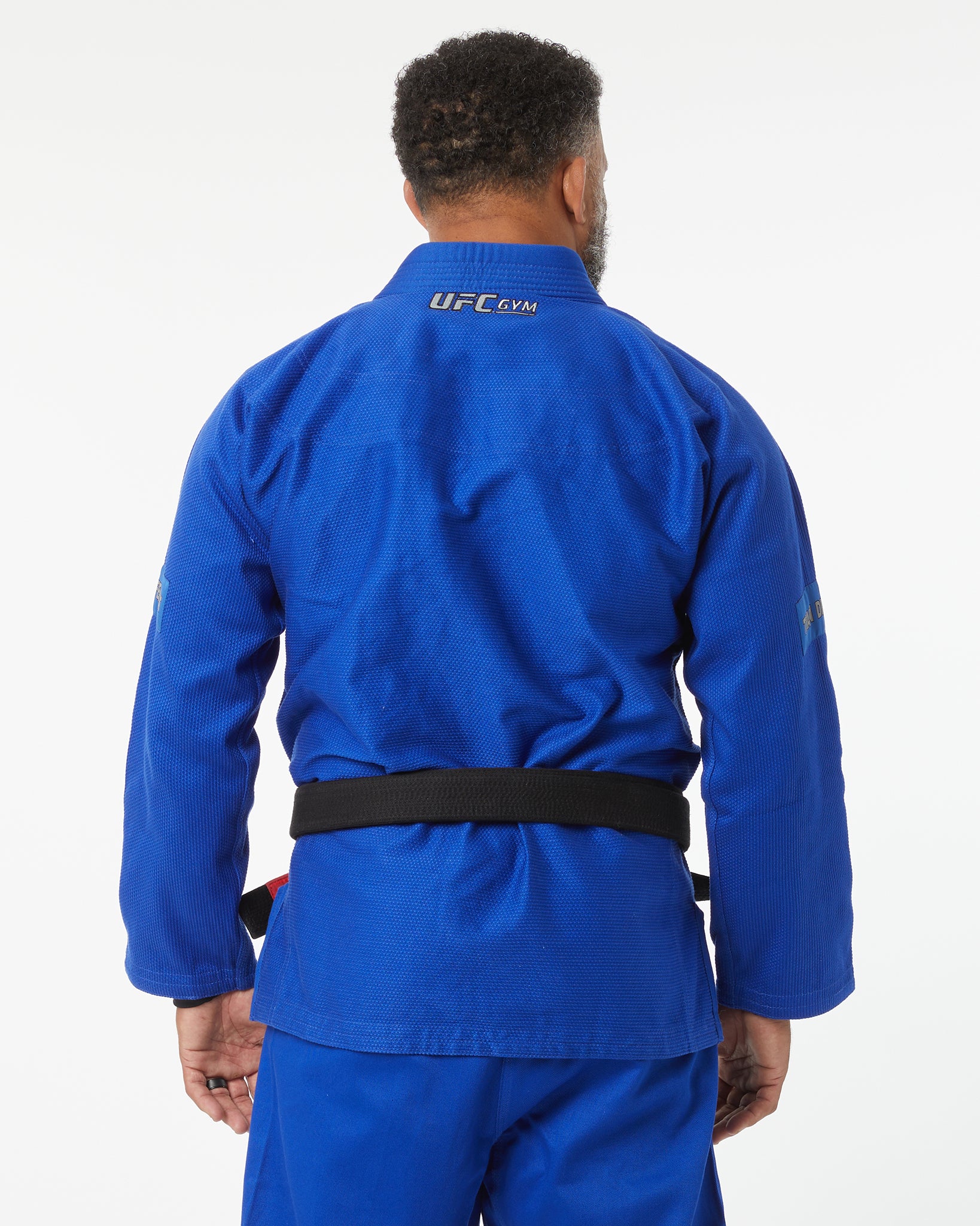 Person wearing a blue UFC Gym gi on a white background facing backward