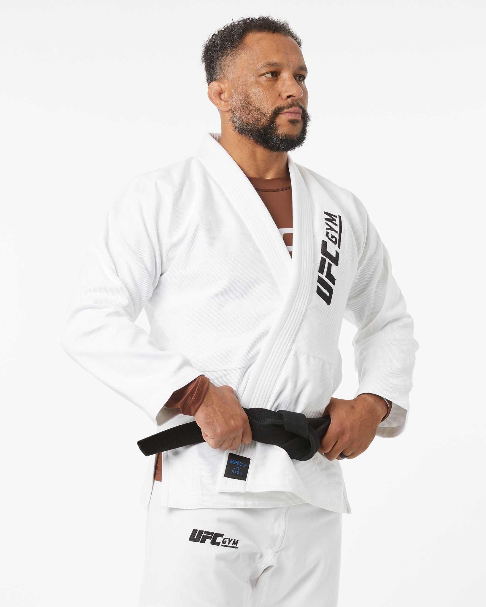Man wearing a white UFC Gym kimono with a black belt on a white background facing right