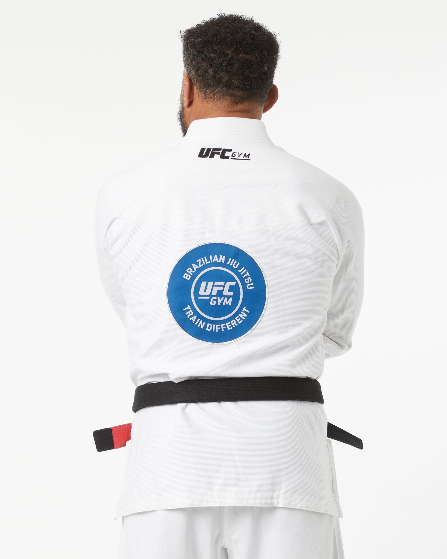 Person wearing a white UFC Gym Brazilian Jiu-Jitsu gi with a blue patch on the back, facing backwards