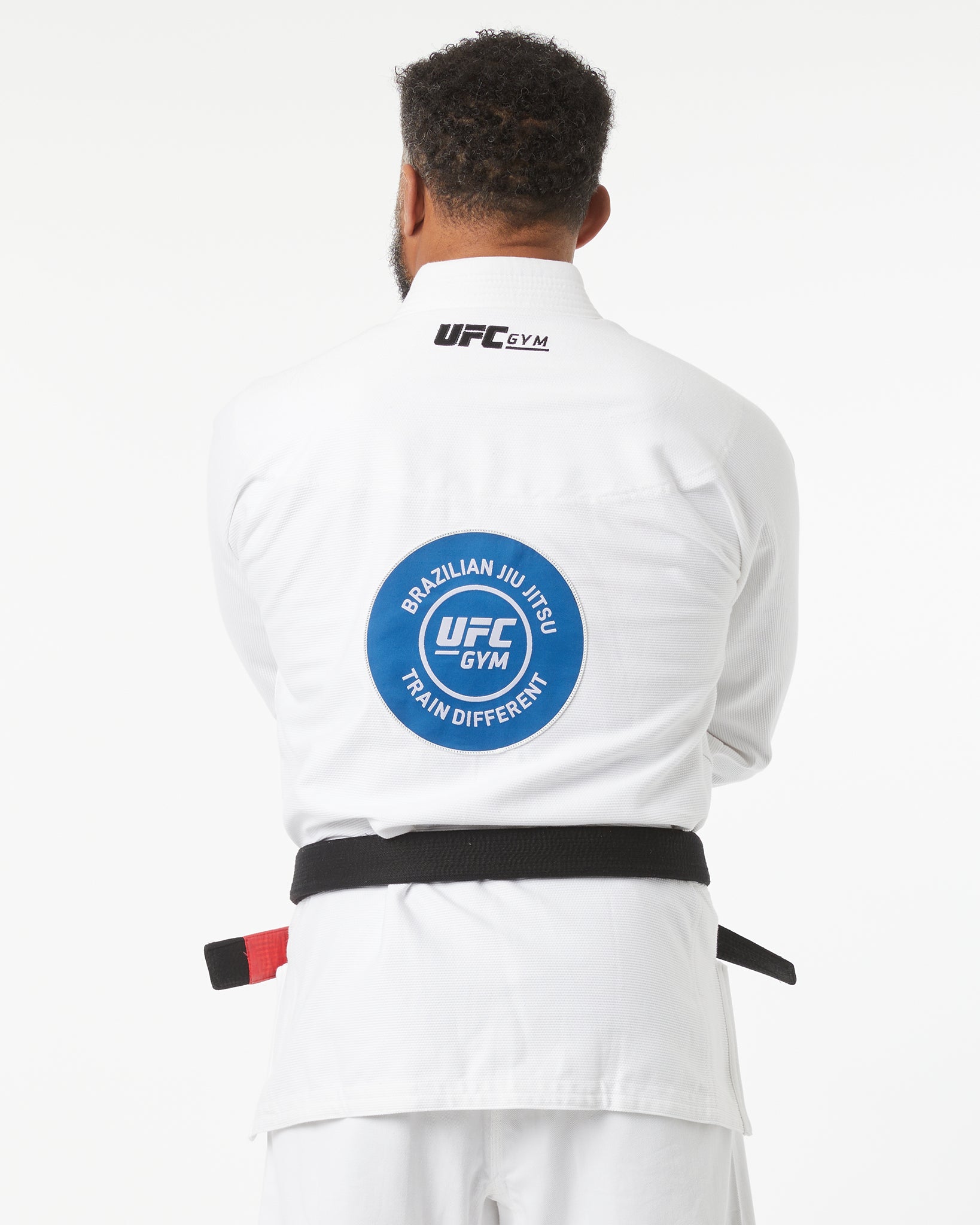 Person wearing a white UFC Gym Brazilian Jiu-Jitsu gi with a blue patch on the back, facing backwards