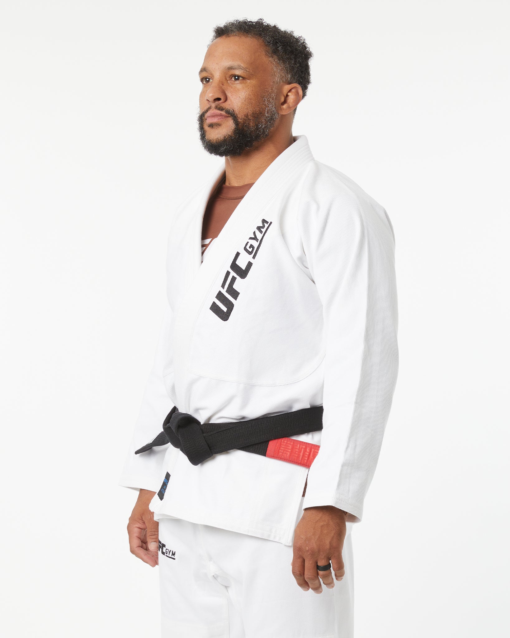 Person wearing a white UFC kimono with a black belt on a white background facing slightly to the left