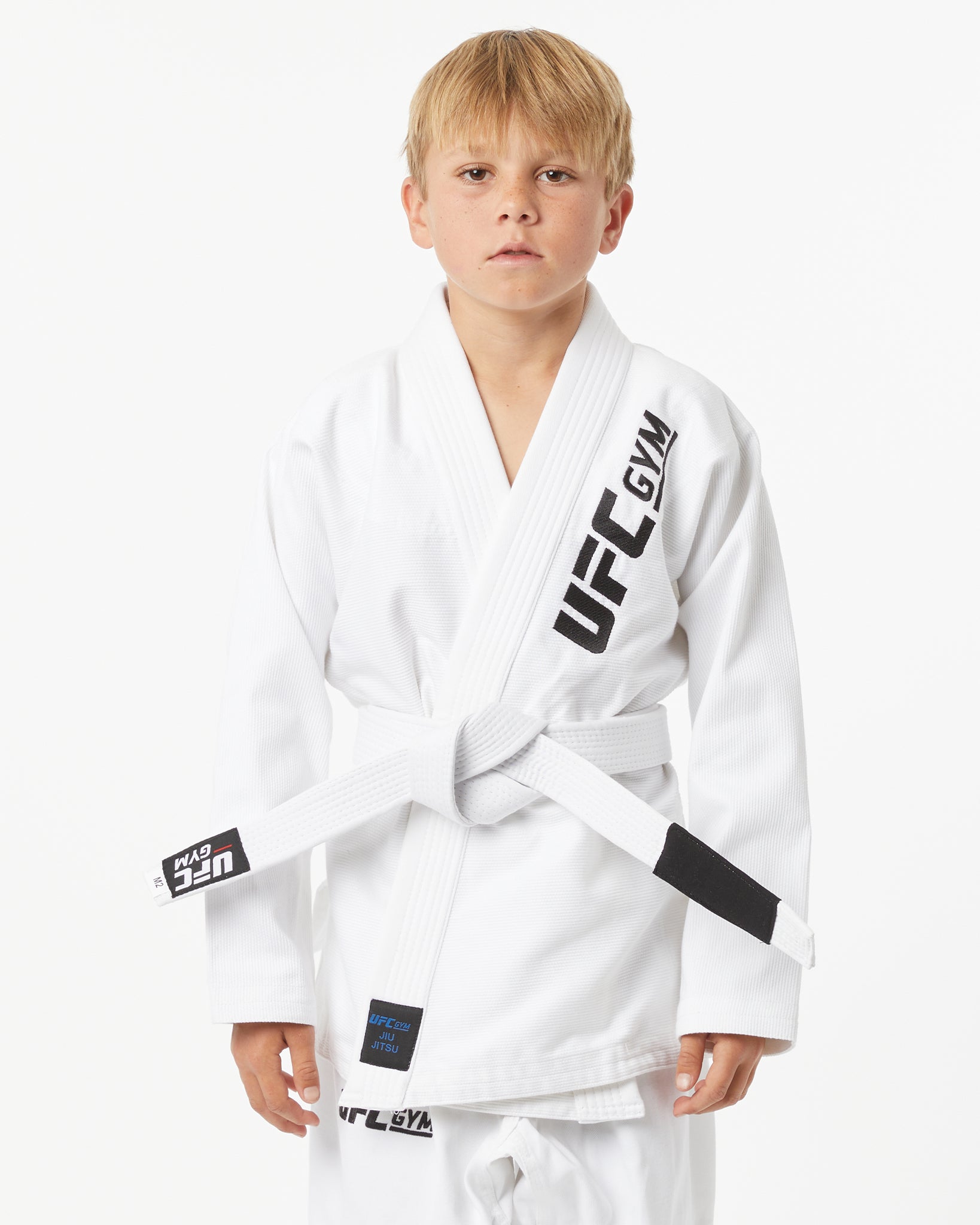 Child wearing a white UFC Gym gi with a white belt on a white background facing forward